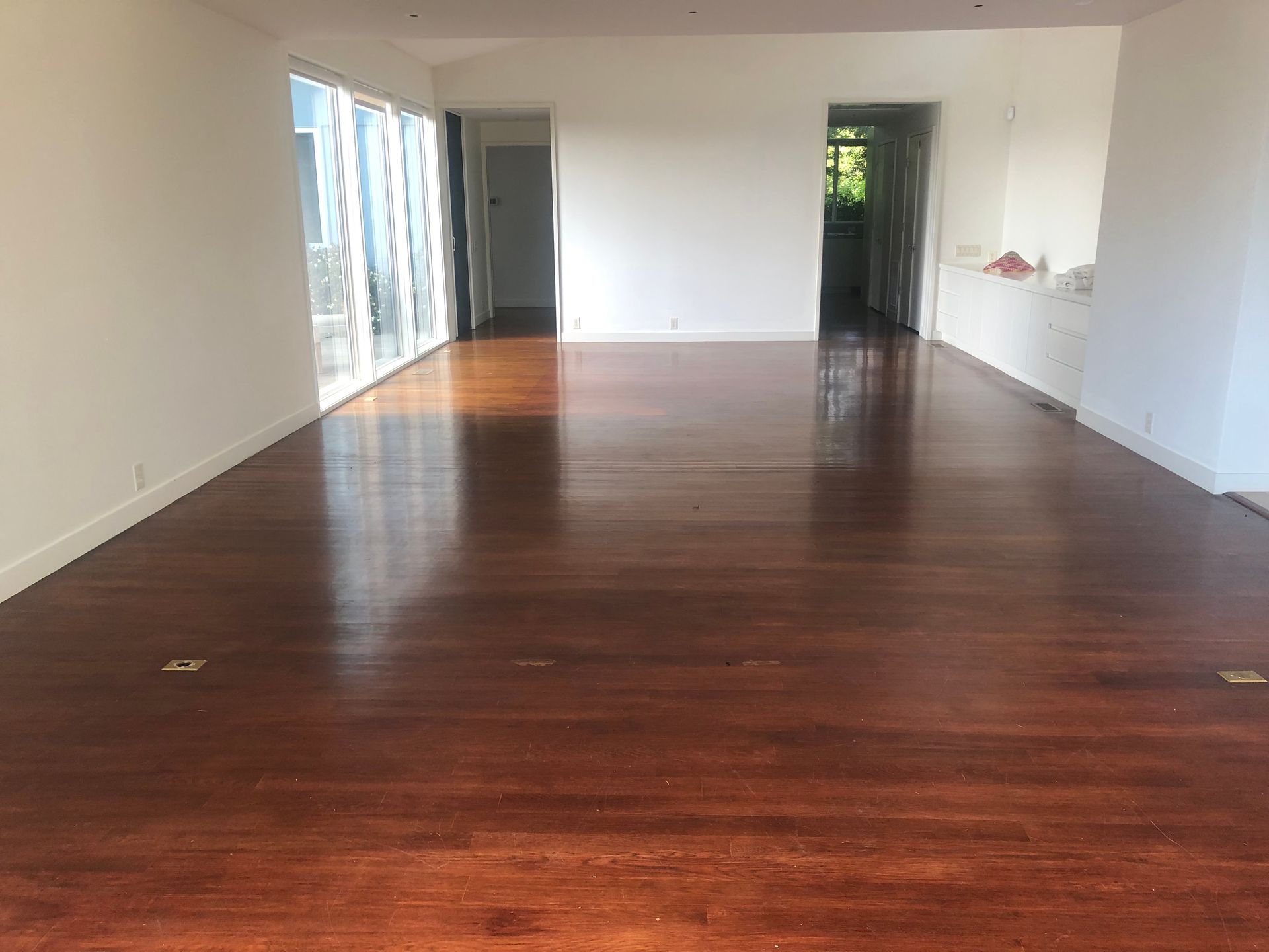 Empty room with polished dark wood floors and white walls. Large windows and doorways.