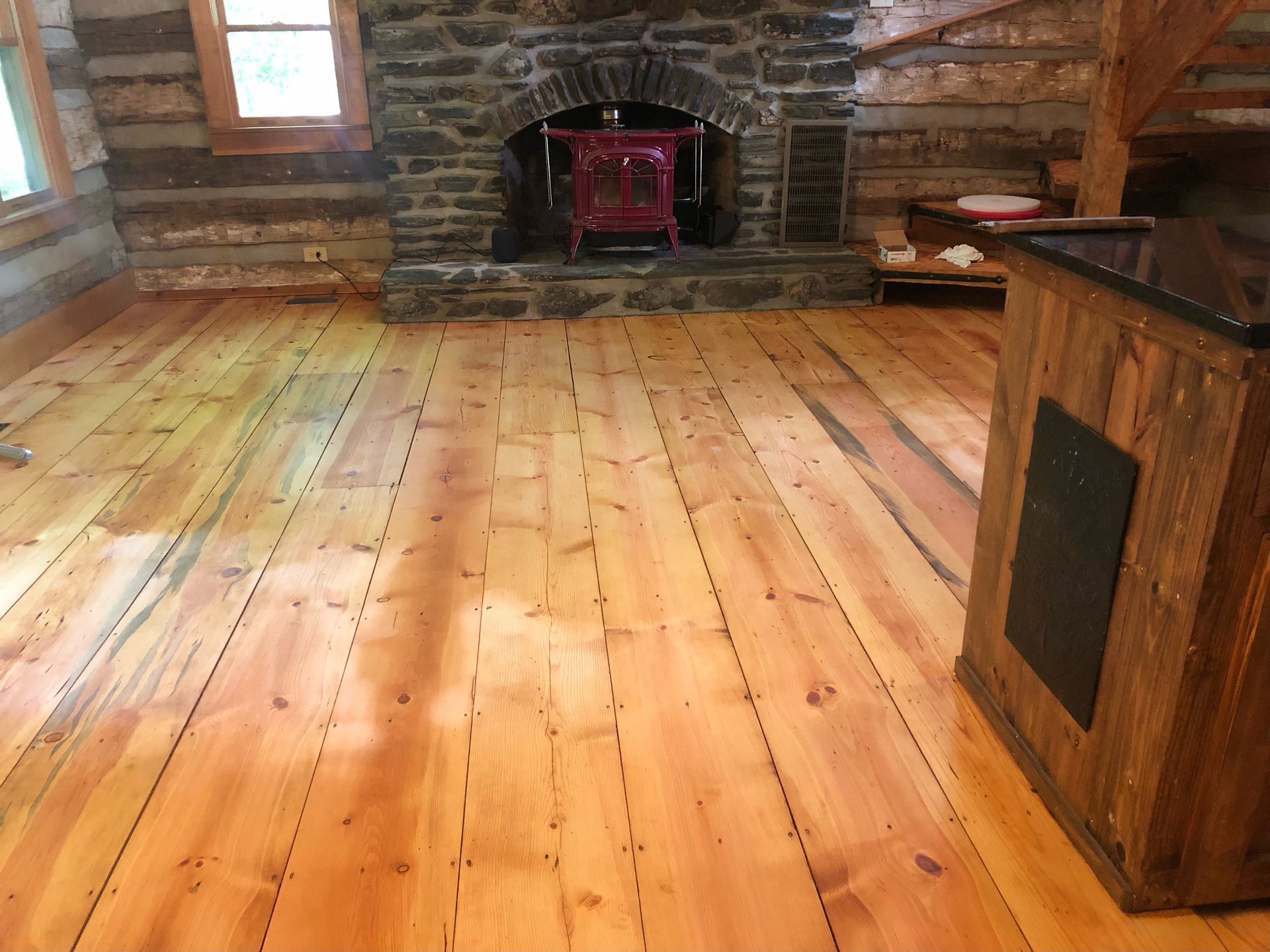 Wide plank hardwood floor in a cabin, with a stone fireplace and wooden cabinetry.