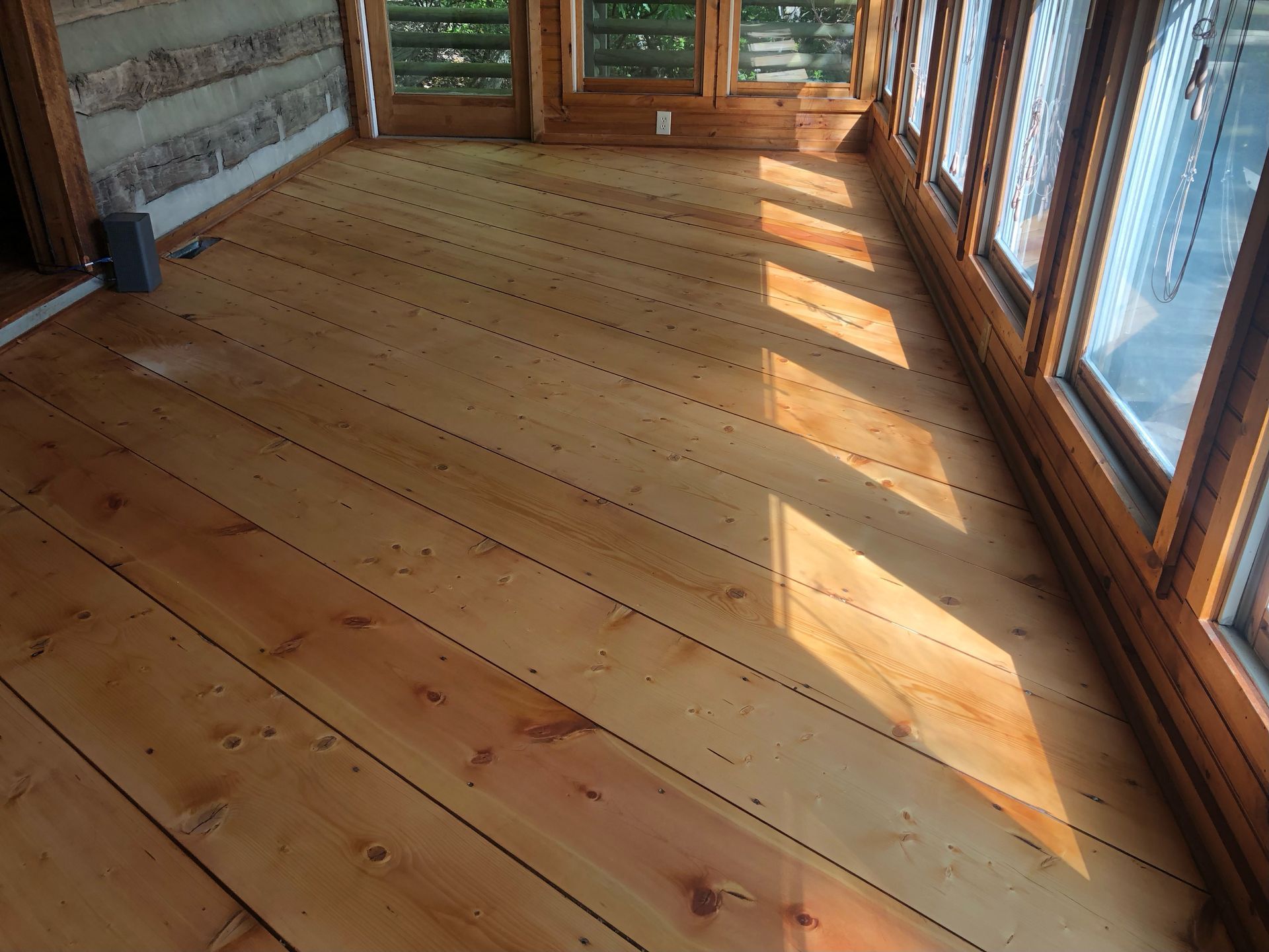 Sunlit hardwood floor with natural oil finish in a room with large windows, light streaming across the planks.