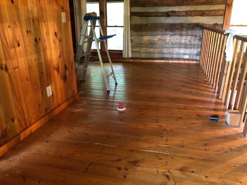 Wooden interior, showing a room with a hardwood floor and log walls. A ladder sits near a window.