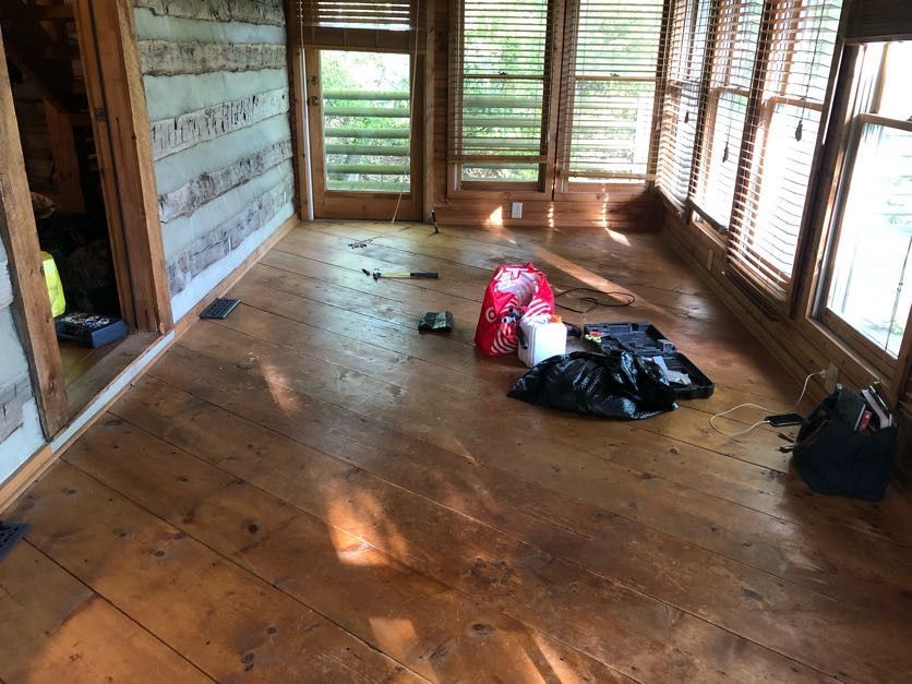 Sunroom with wood floors, log walls, and windows, cluttered with trash bags and tools.