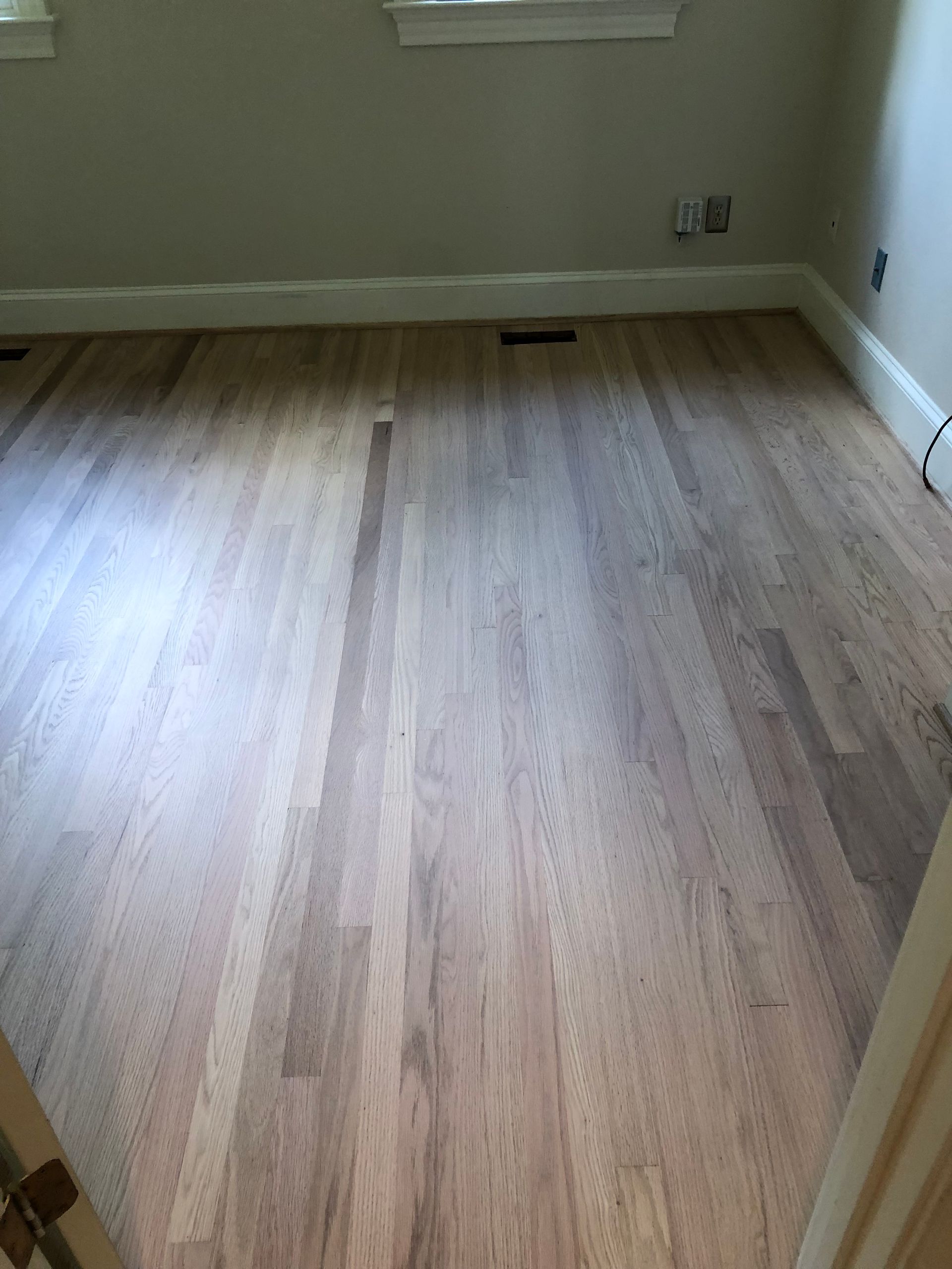Wooden floor in a room, with white baseboards and light-colored walls.