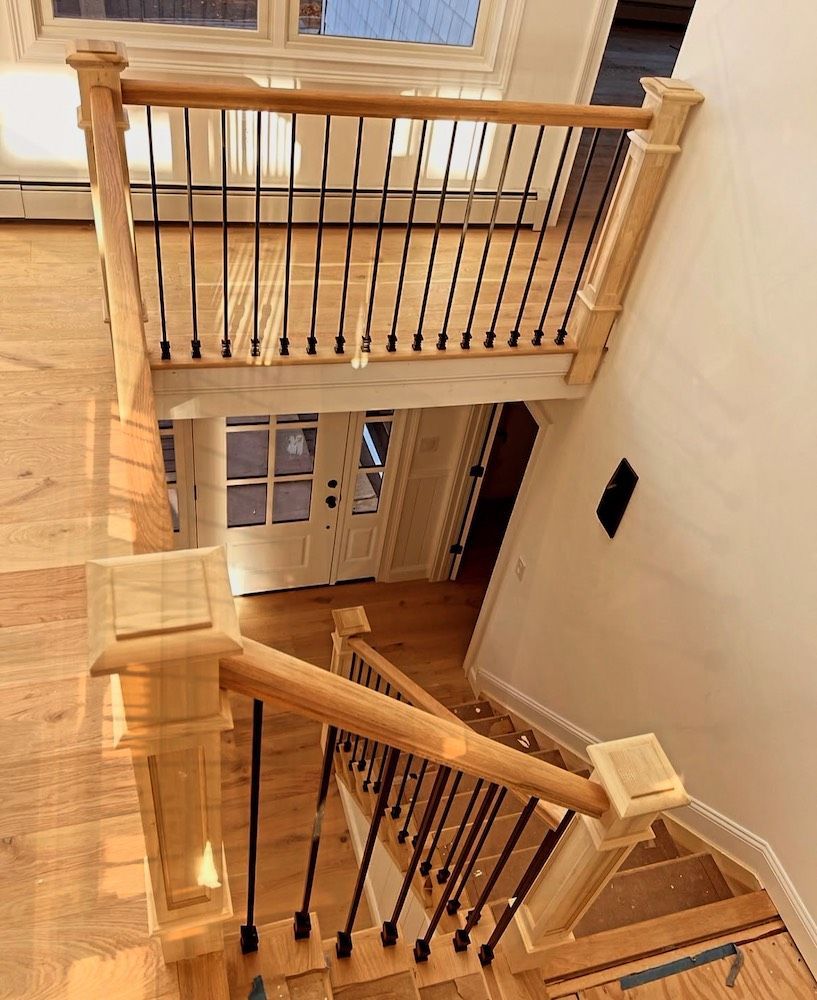 Wooden staircase with black metal railings, leading to a front door. Light wood floors and walls.