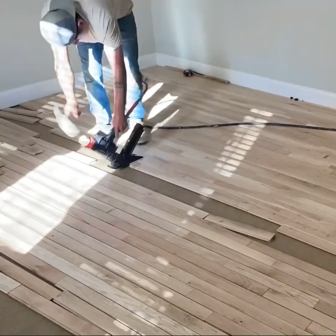 Person installing hardwood flooring with a nail gun in a room. Local hardwood floor installers Raleigh NC.