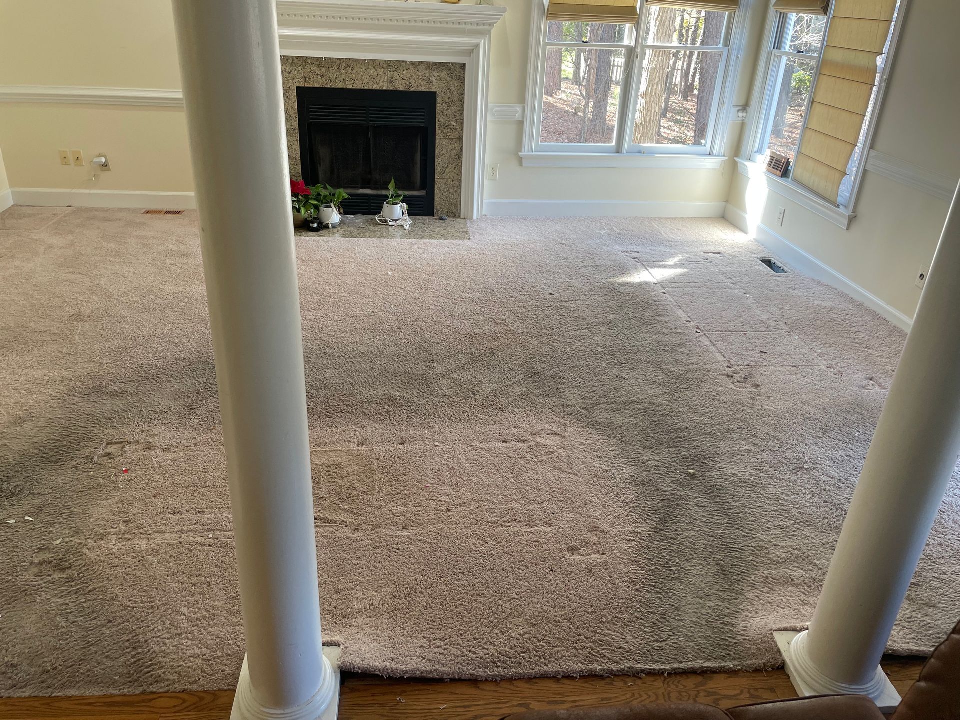 Beige carpeted room with fireplace, windows, and white columns.