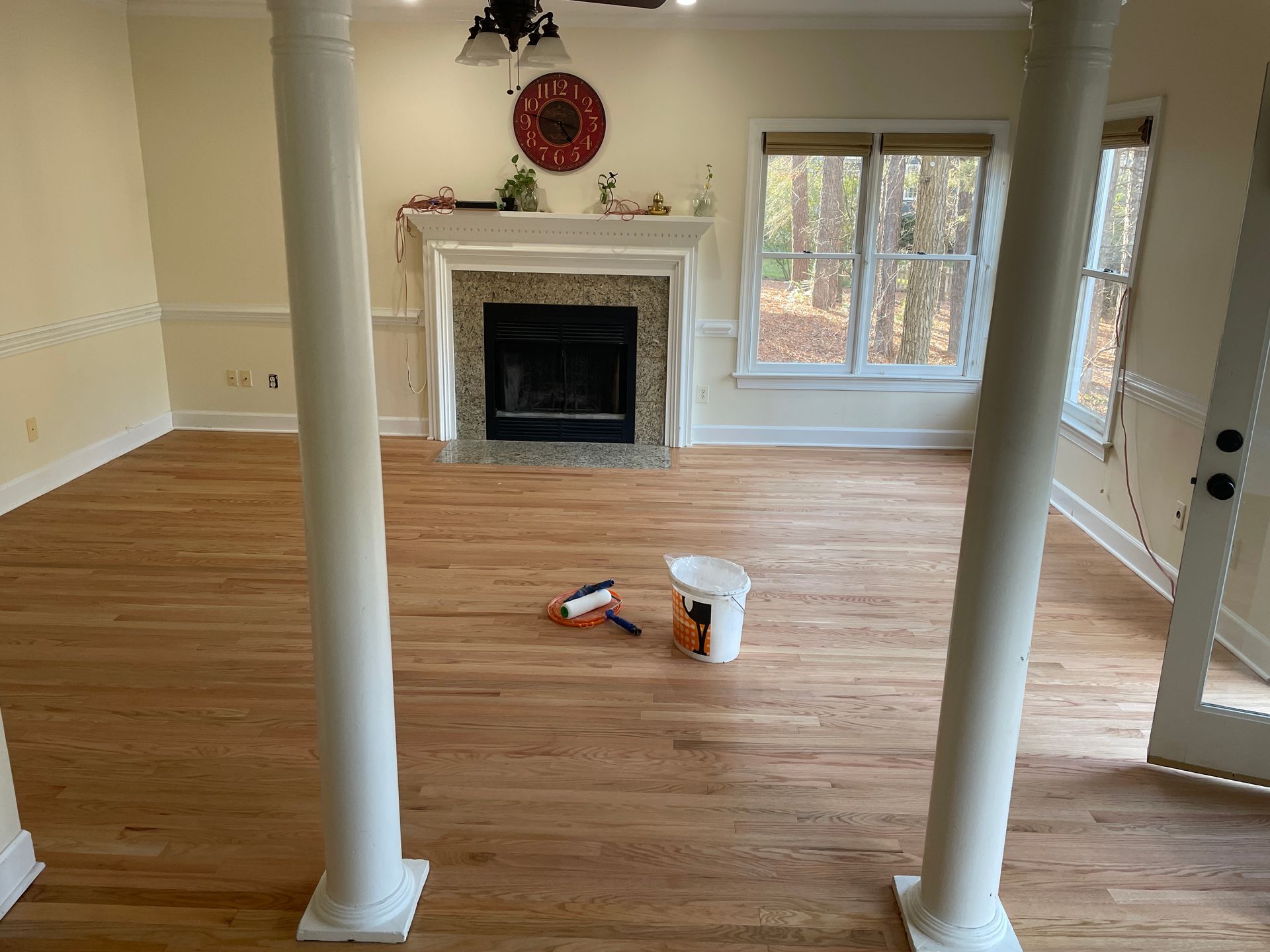 Natural oil finish hardwood floor in living room with fireplace and columns. Bucket and roller on floor.