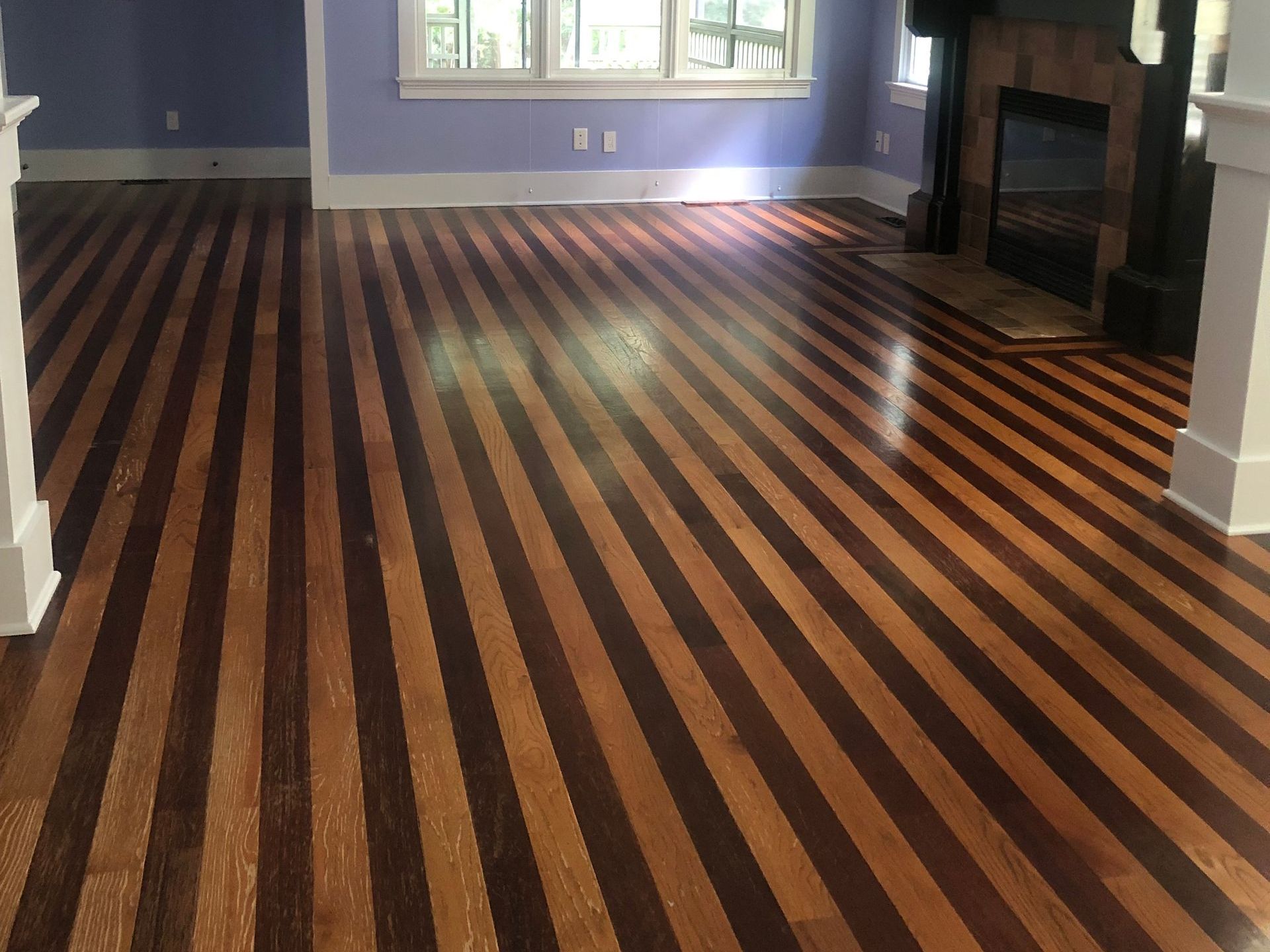 Striped hardwood floor in a room with a fireplace and light blue walls. Before sanding and refinishing