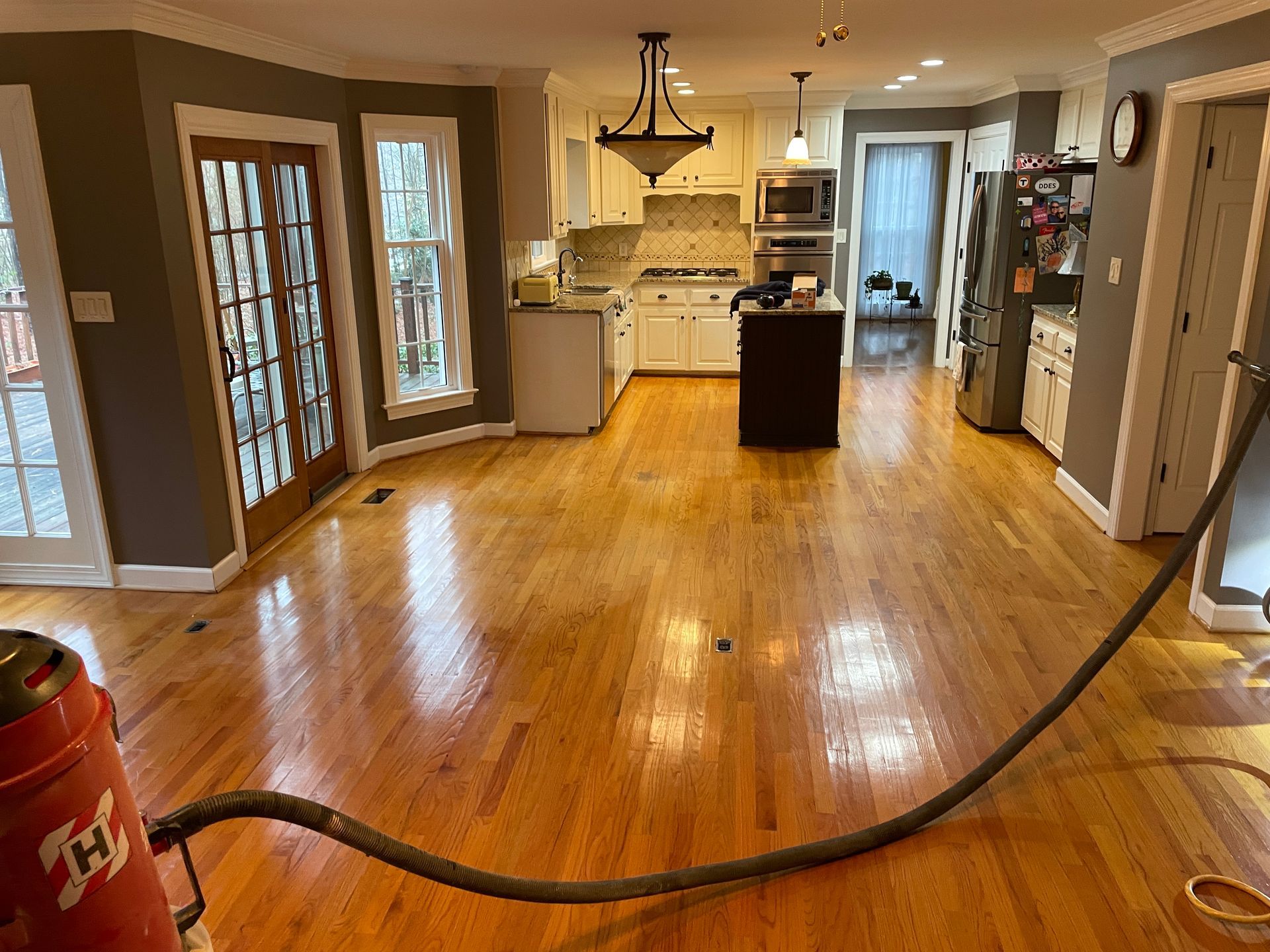 Wooden floors being refinished in a home, showing a kitchen, a hose connected to a red machine.