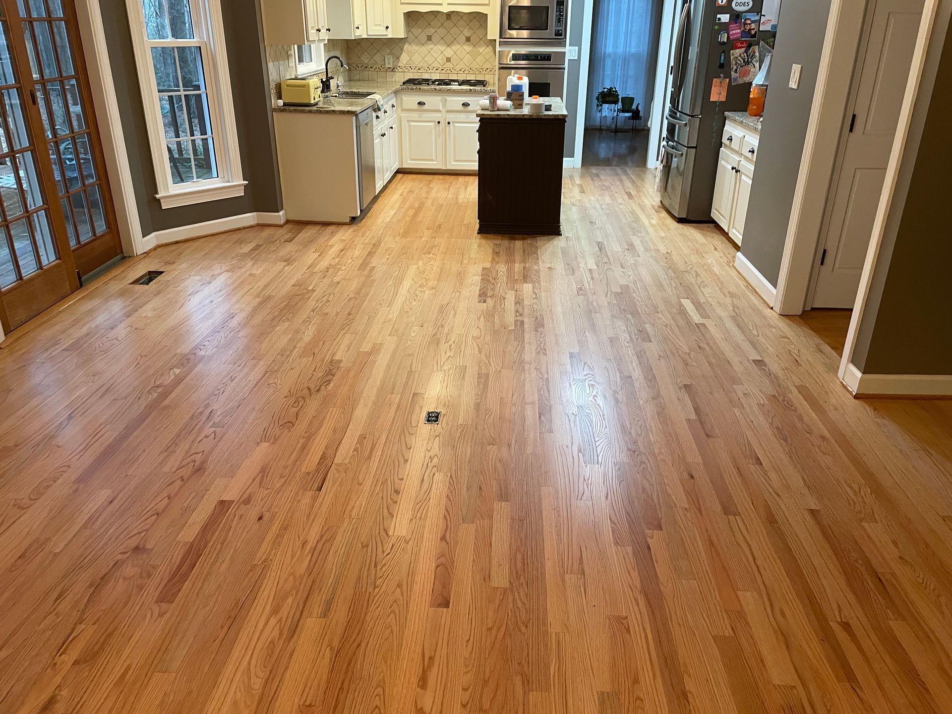 Hardwood floor refinishing in a kitchen with white cabinets, an island, and access to a patio.
