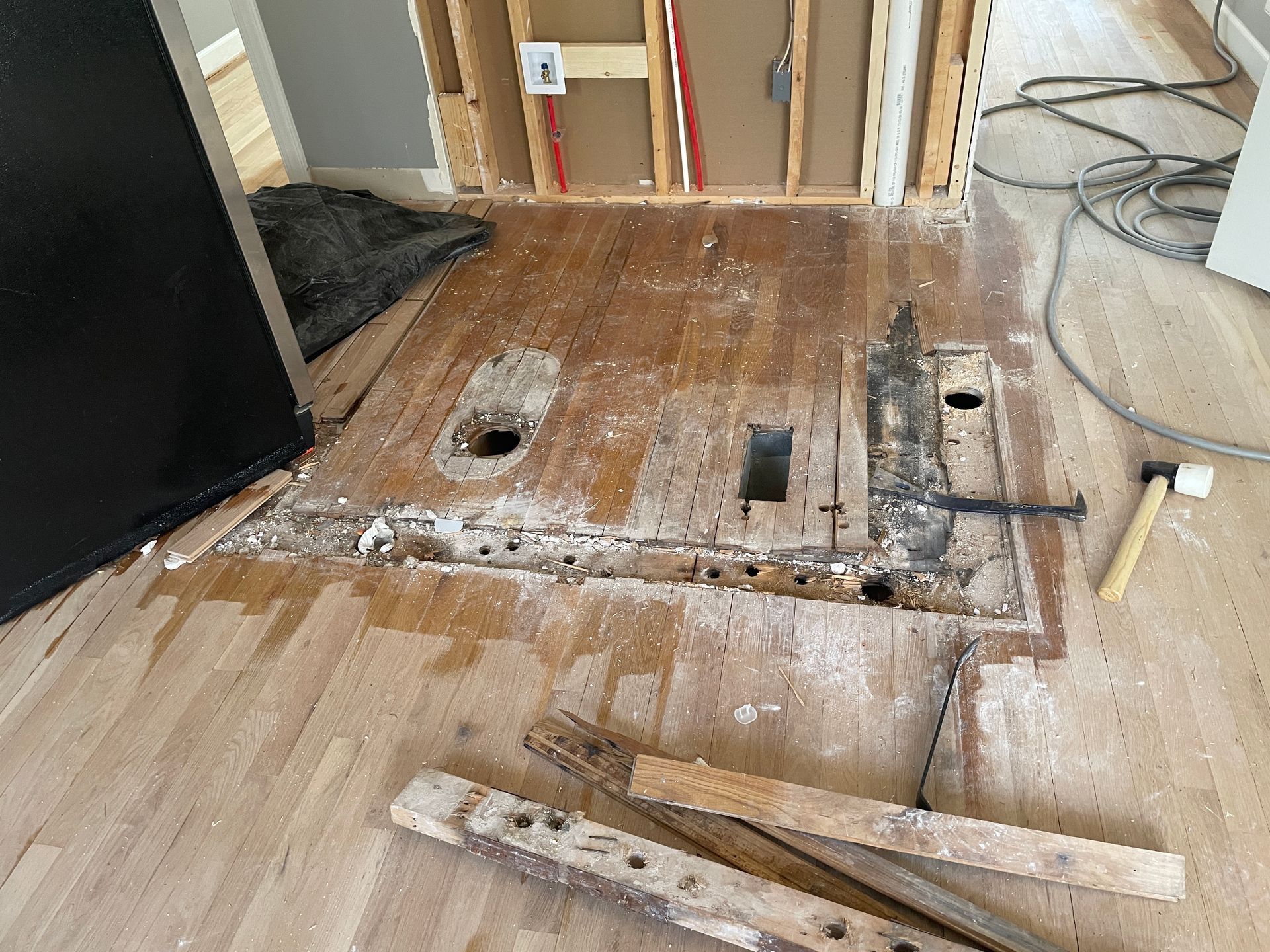Hardwood floor with section removed, exposing subfloor, tools scattered. Renovation in progress.