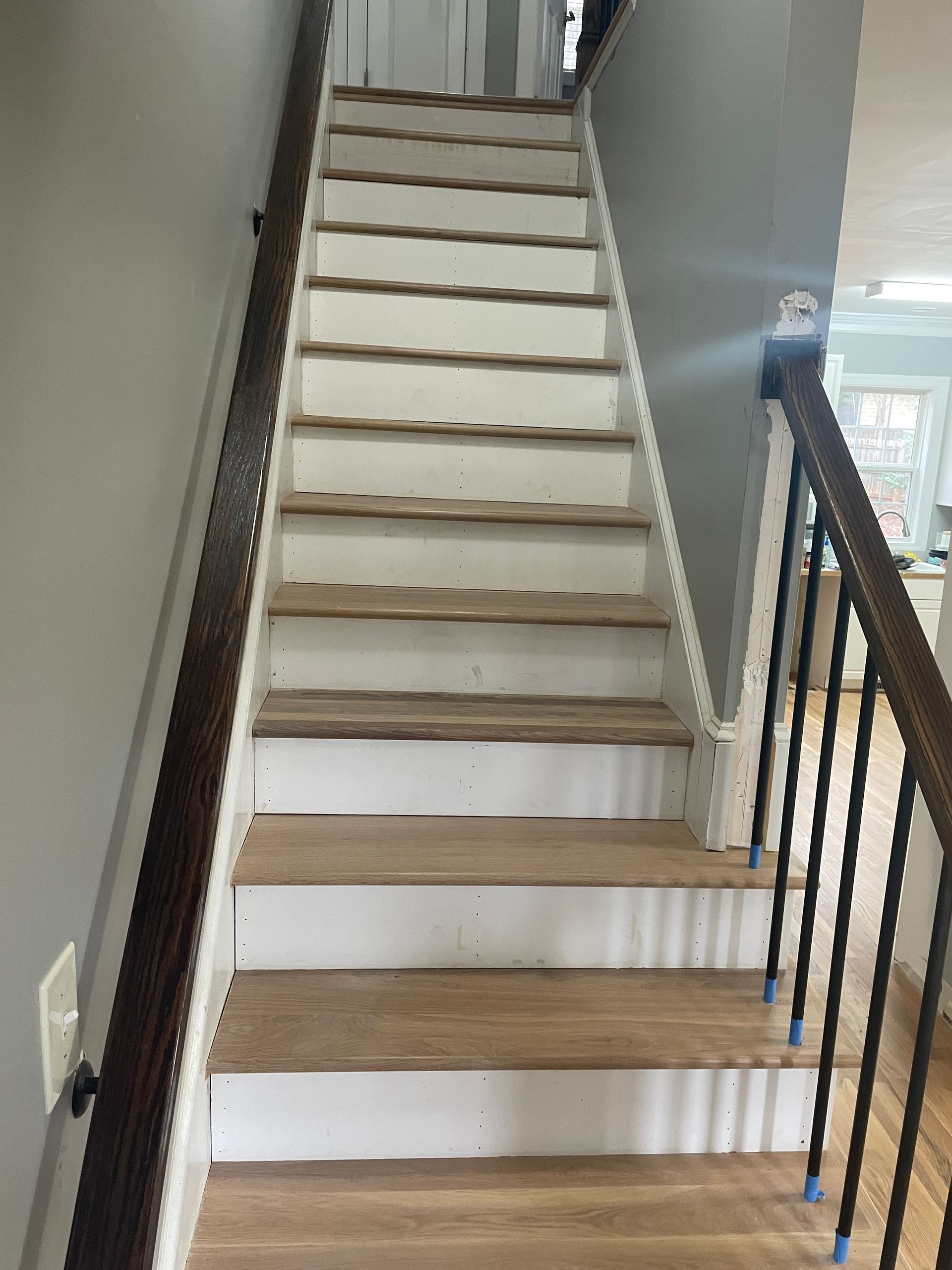 A white staircase with wooden steps and a black railing in a house.