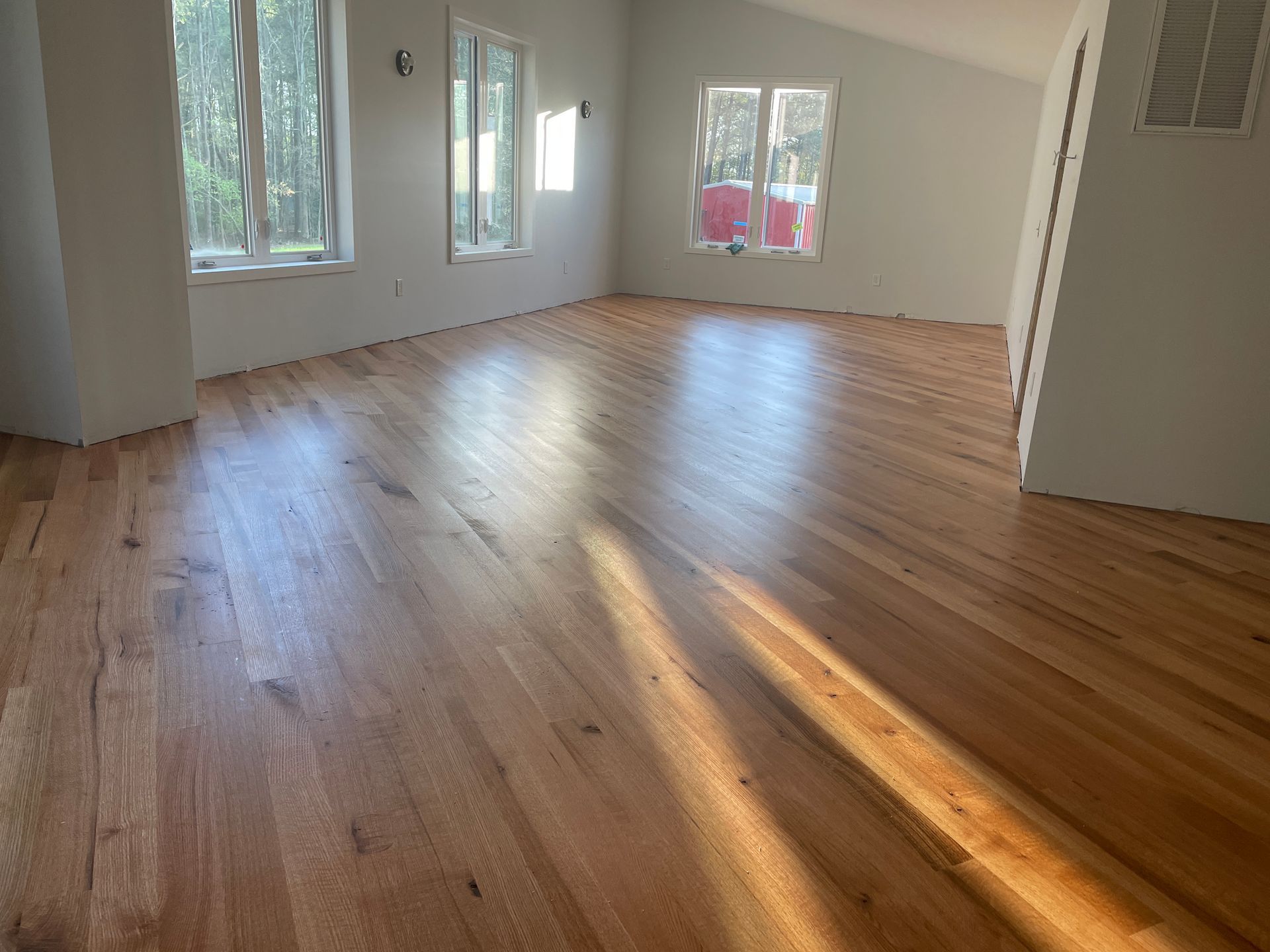 Light-filled room with newly finished hardwood floors and several windows.