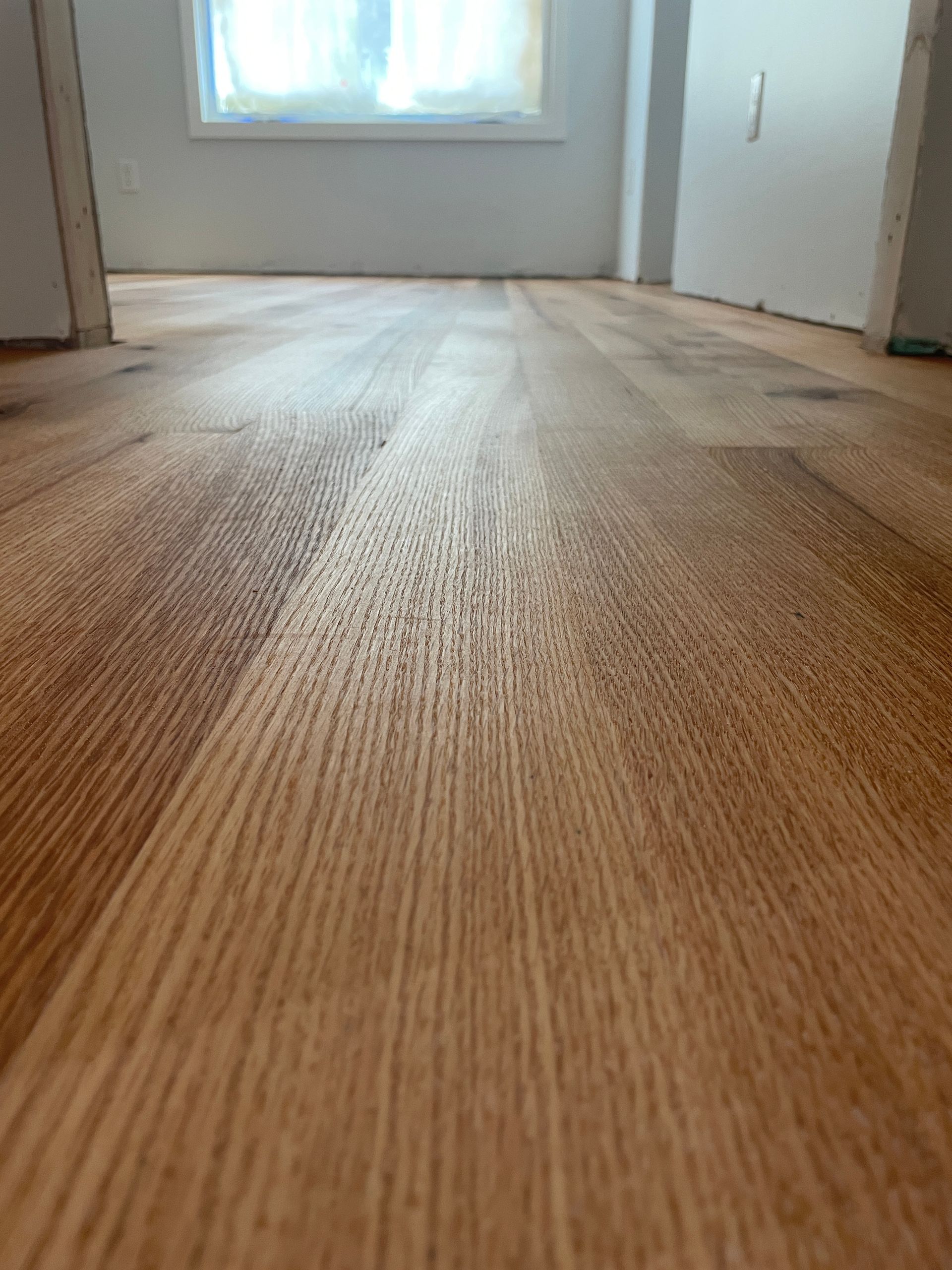 Close-up of newly installed wood floor in a room with a window, showcasing the wood grain and color variations.