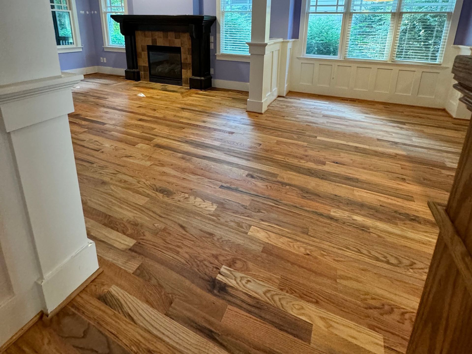 Hardwood floors refinished with natural oil in a room with a fireplace and windows, showcasing natural wood tones and light.