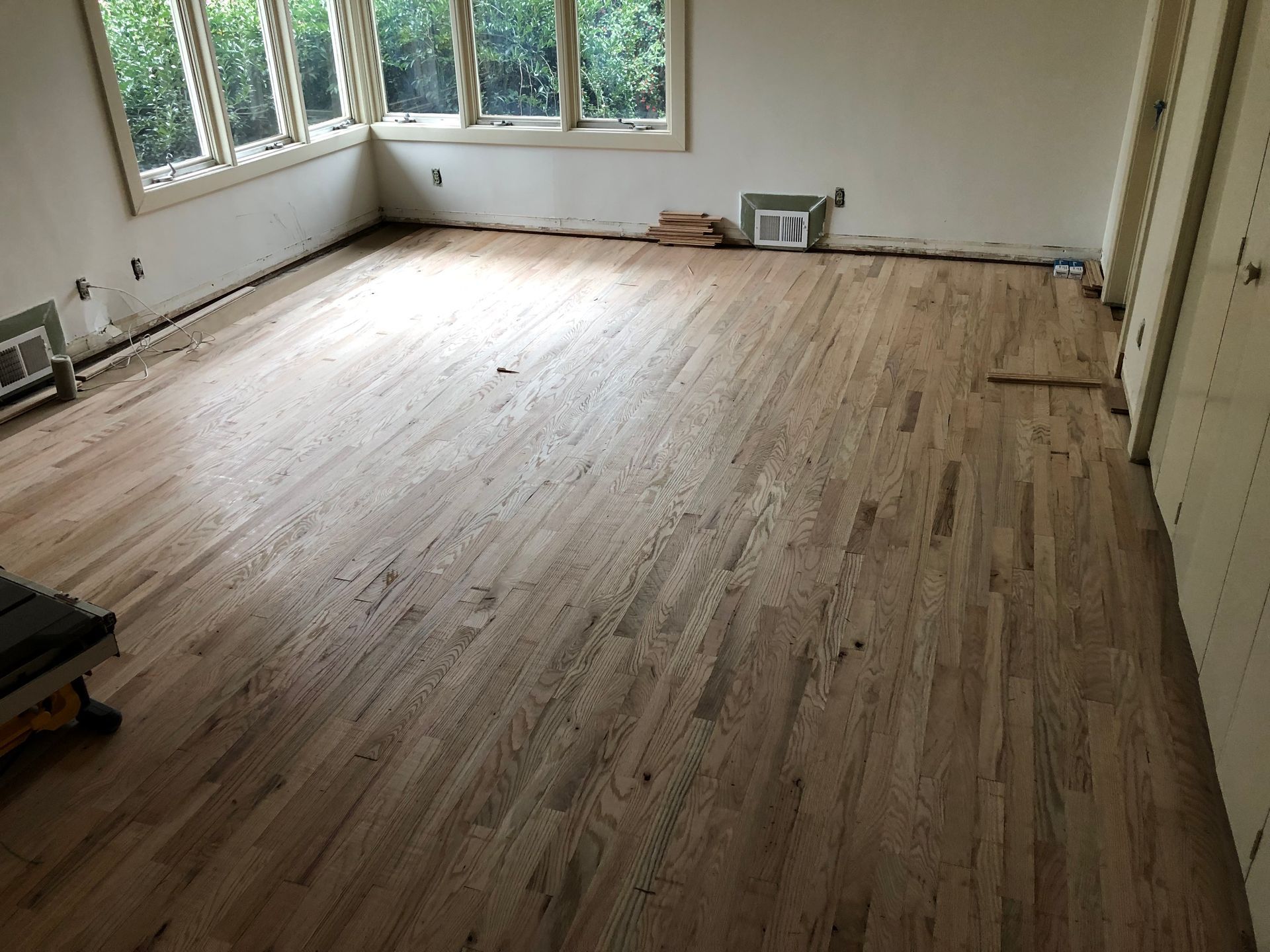 Hardwood floor in an empty room, near windows and a closed door. Light brown color.