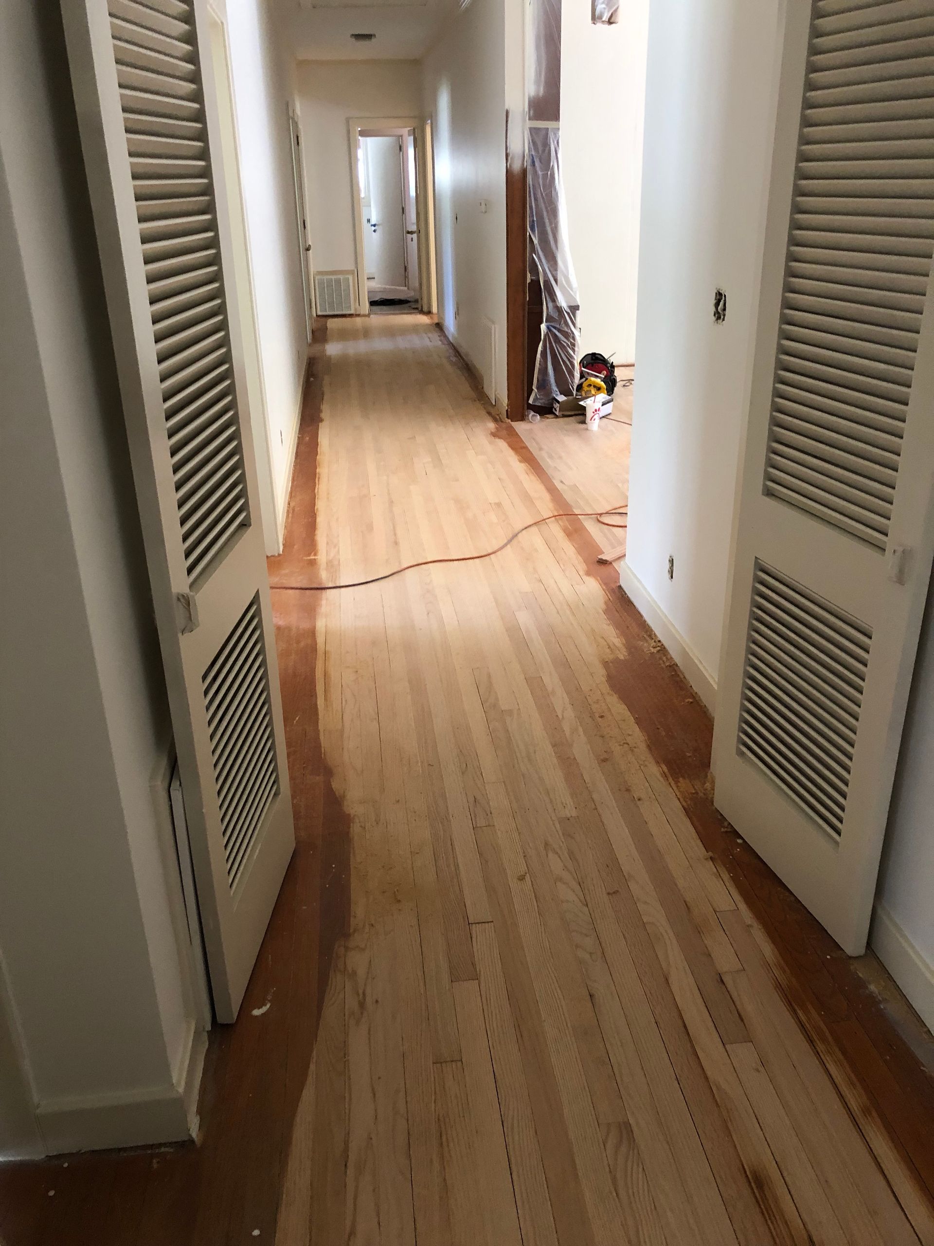 Hallway with wood floors, doors with white louvered panels. Some floors have a dark stain. Hardwood floor refinishing.