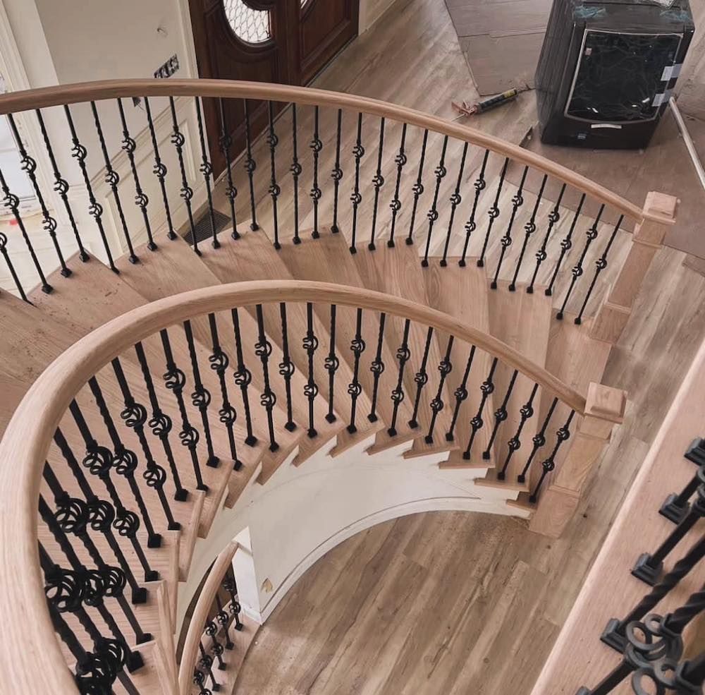 Wooden curved staircase with black iron railings.