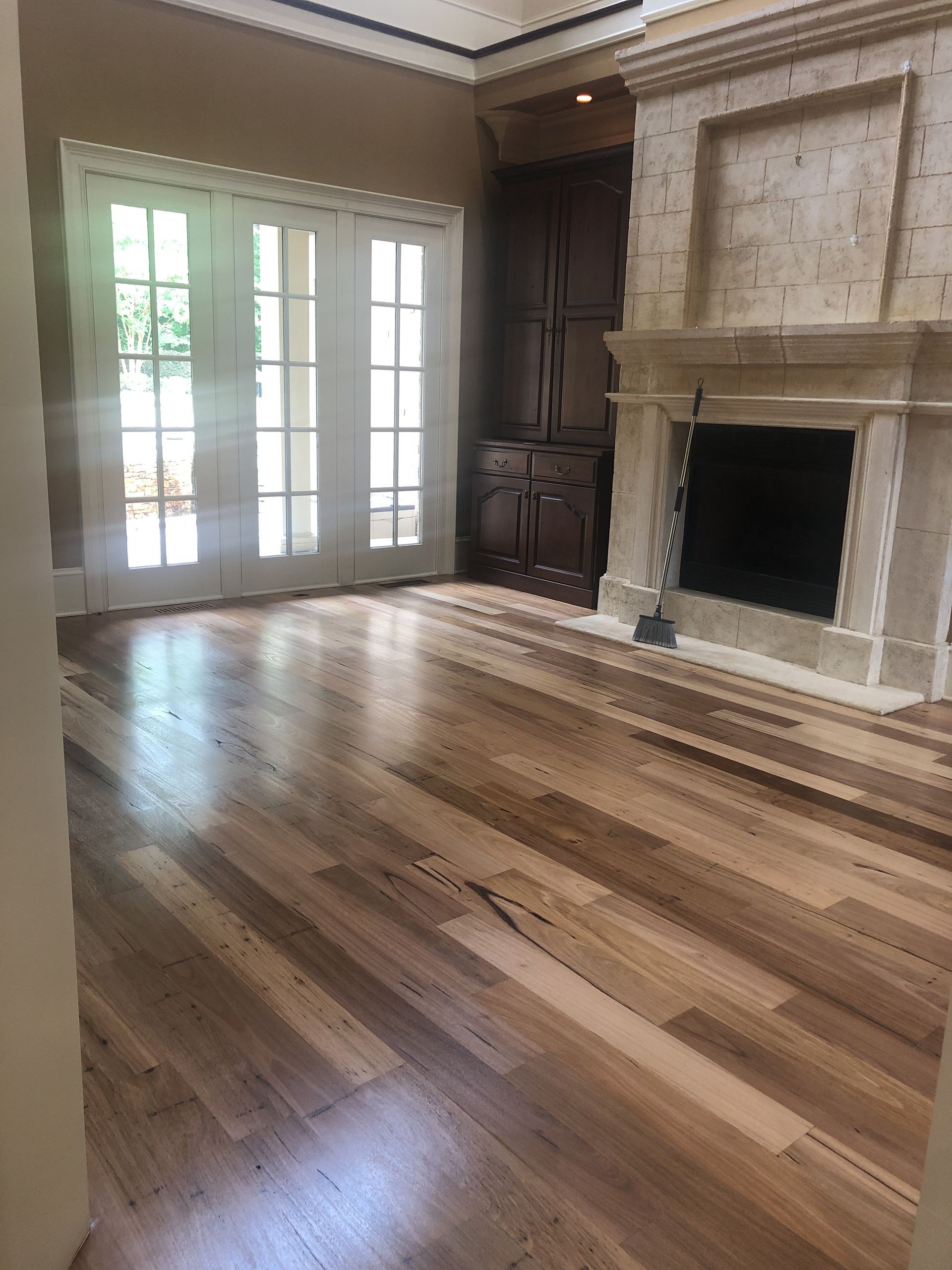 Hardwood floor in room with French doors, built-in cabinet, and stone fireplace.