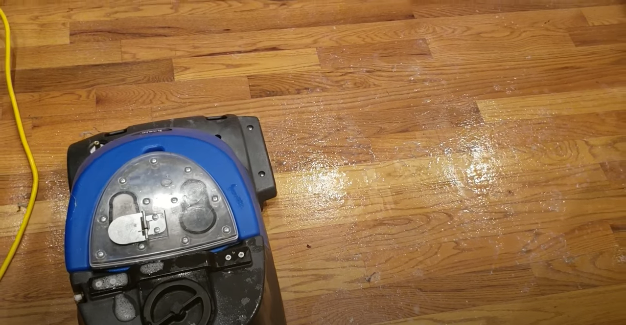 Vacuum cleaner on hardwood floor with white debris.