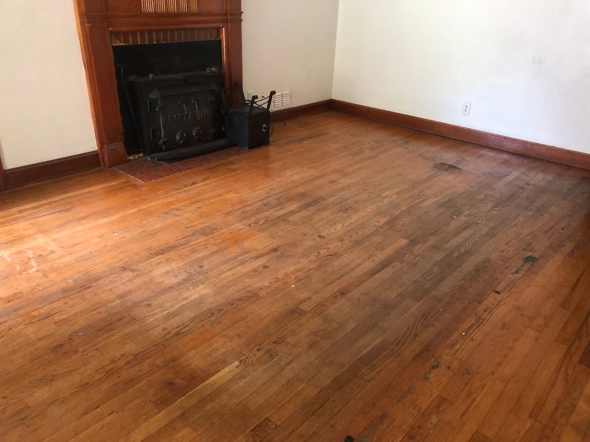 An empty living room with worn hardwood floors and a fireplace.