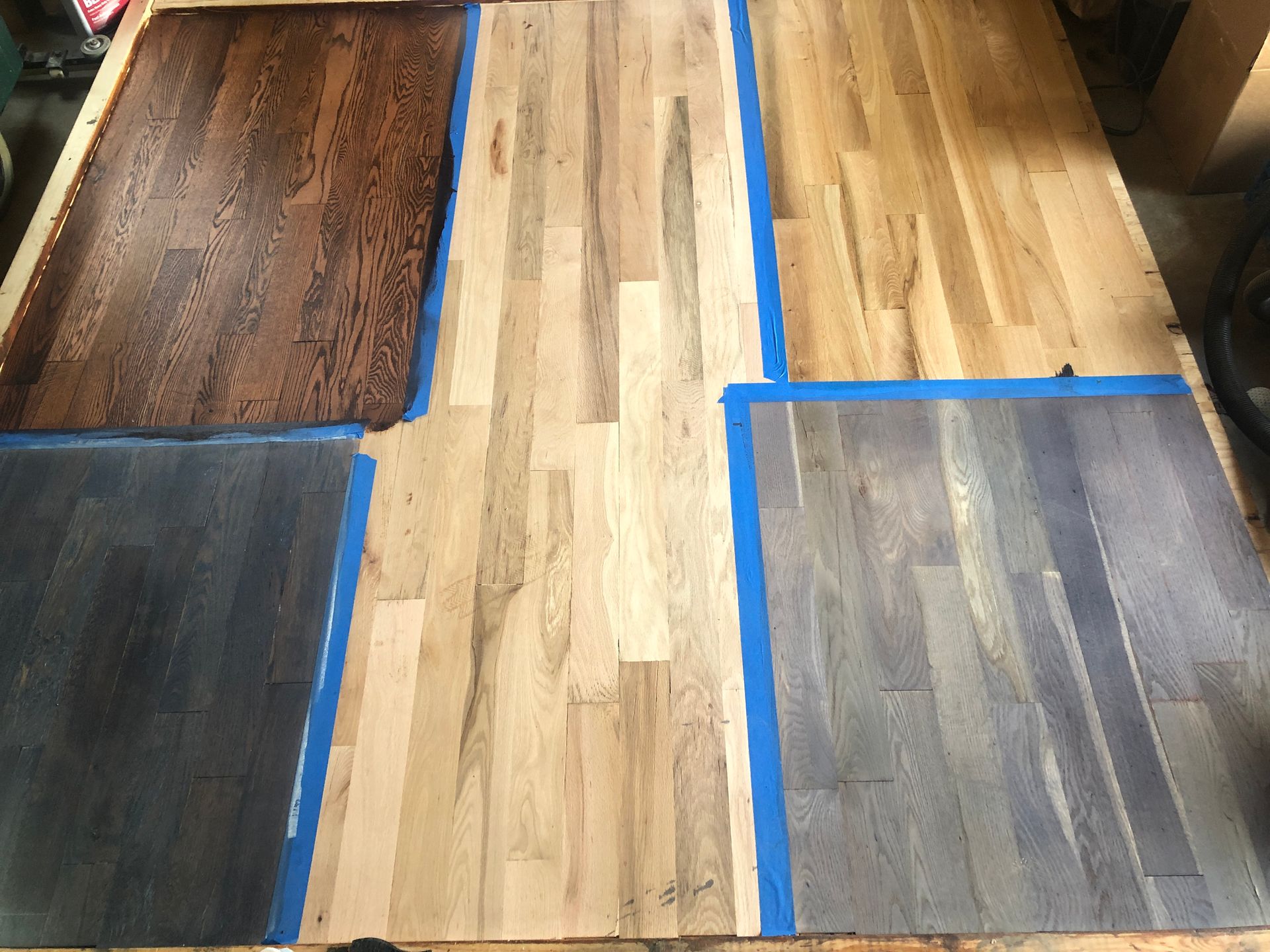 Wooden floor stain samples: dark brown, natural, gray-blue. Blue tape sections show the different stain colors.