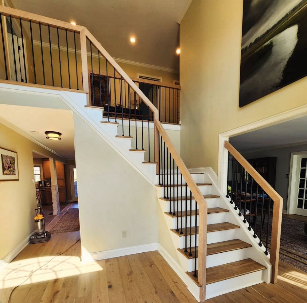 A staircase with wooden steps, black iron railings, and a landing, bathed in natural light. Stair installation.