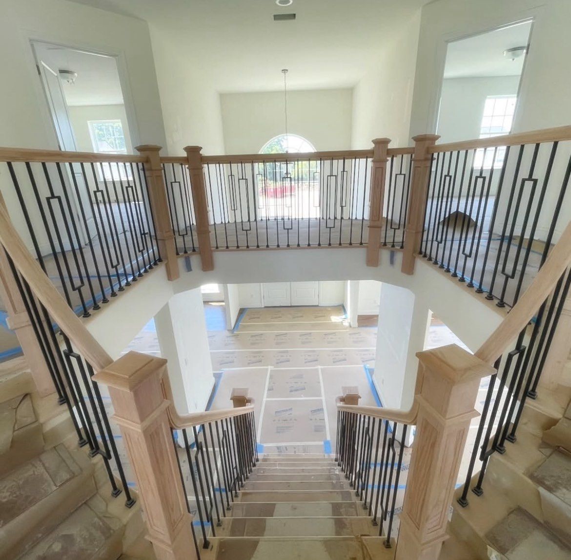Interior view of a staircase with light wood railing, black metal balusters, and large mirrors. Stair installation company.