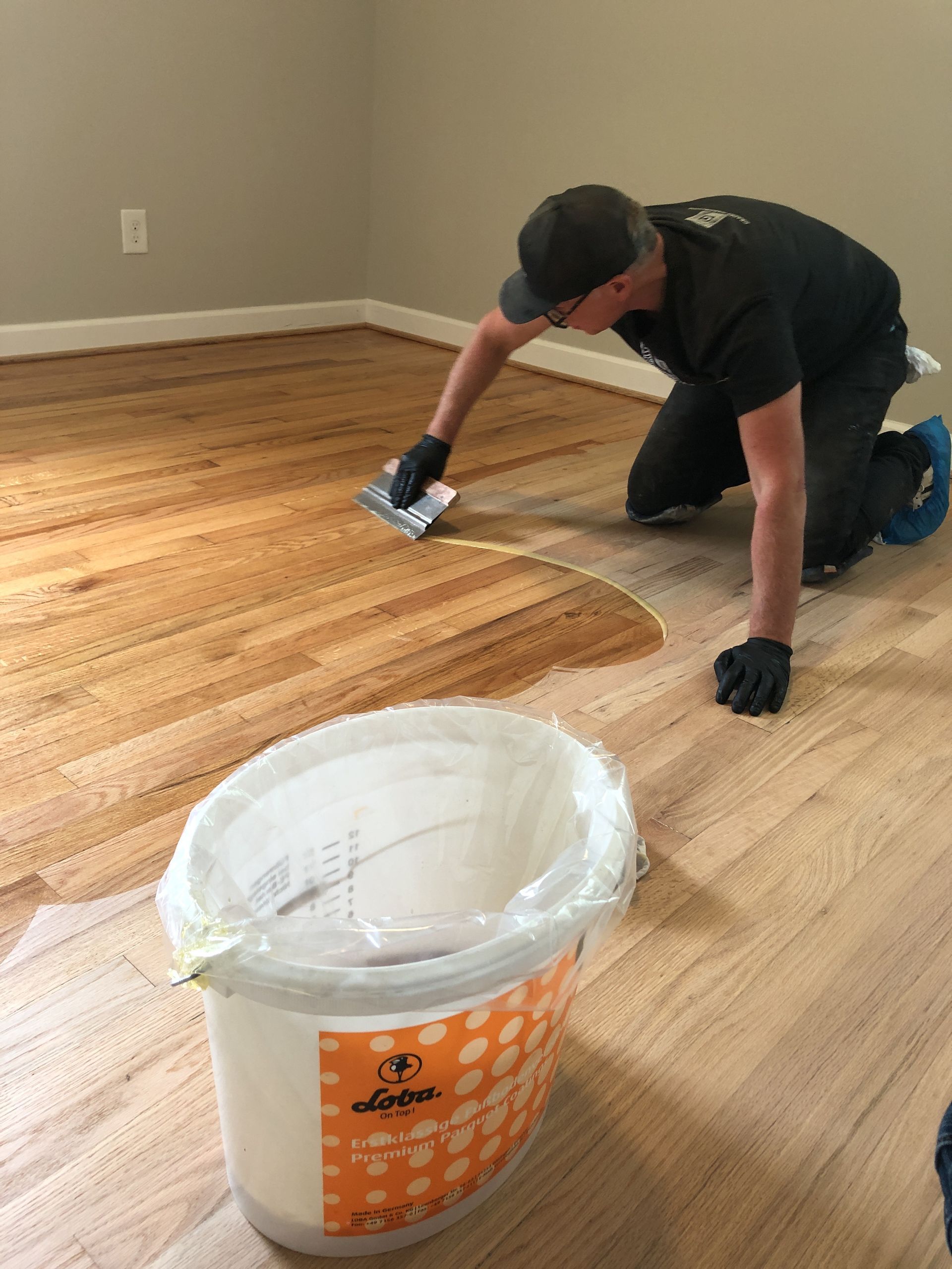 Professional hardwood flooring contractor applying finish to hardwood floor in a room, using a trowel.