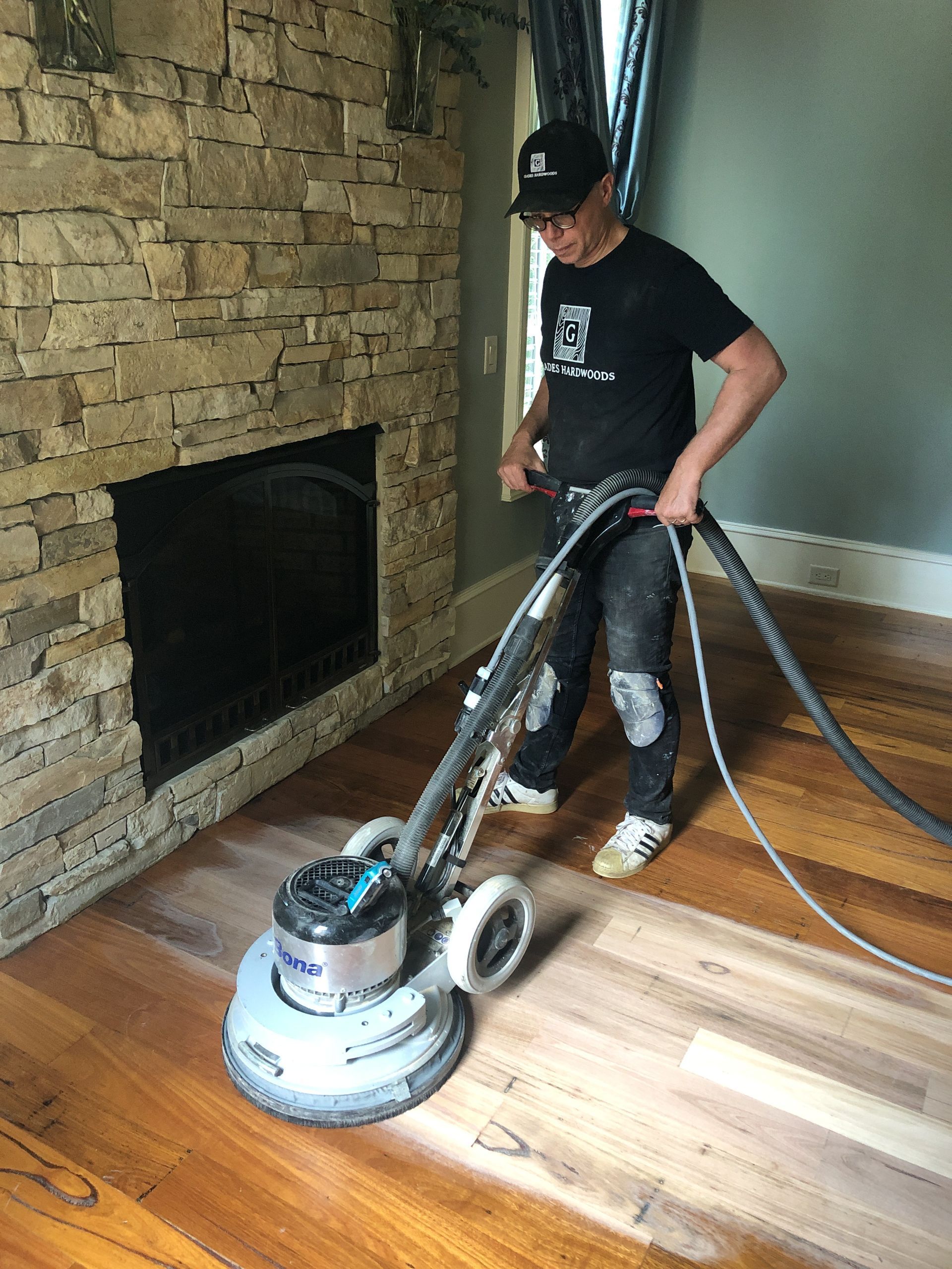 Professional hardwood flooring contractor in Raleigh sanding hardwood floor near a stone fireplace, holding a floor sander.