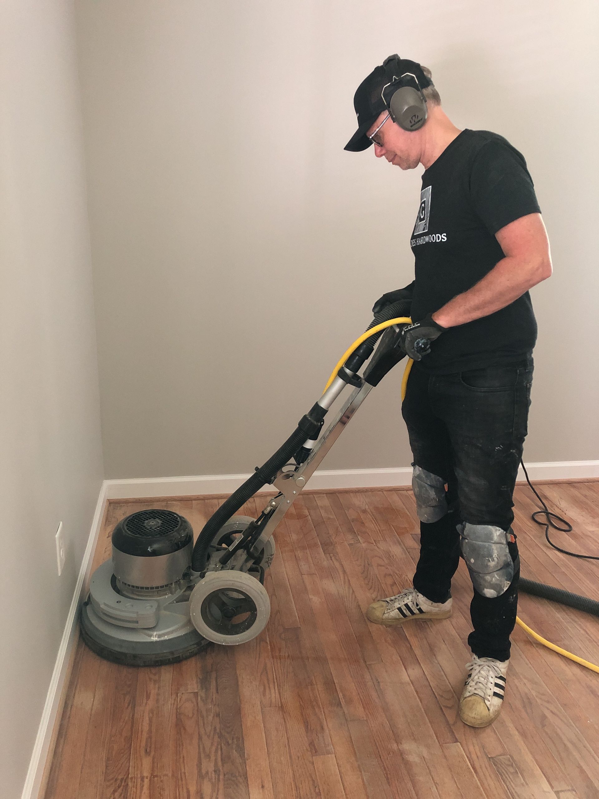 A man sanding is using a sander on a wooden floor.