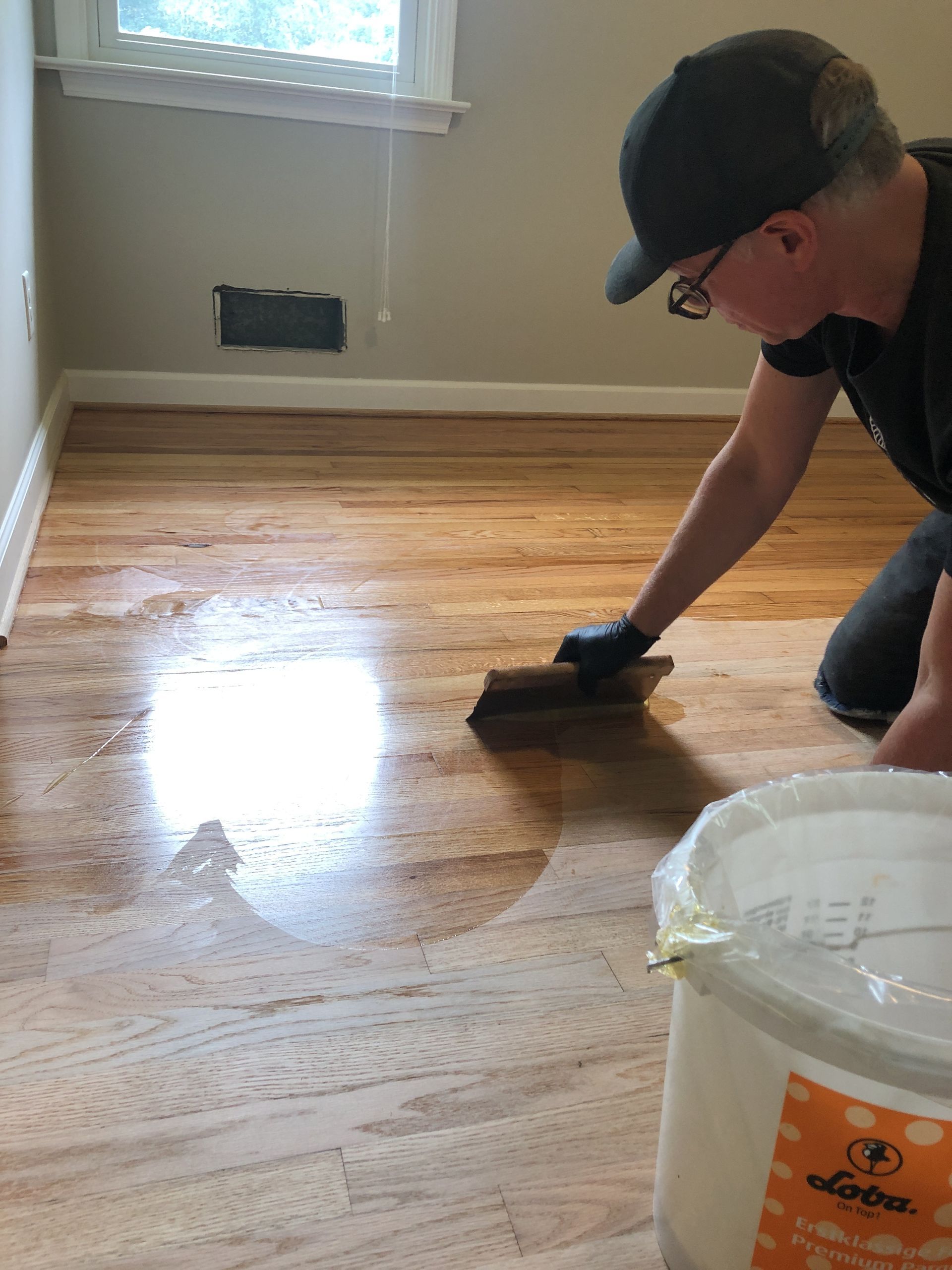 A man is troweling on and applying a natural oil finish to a wooden floor.