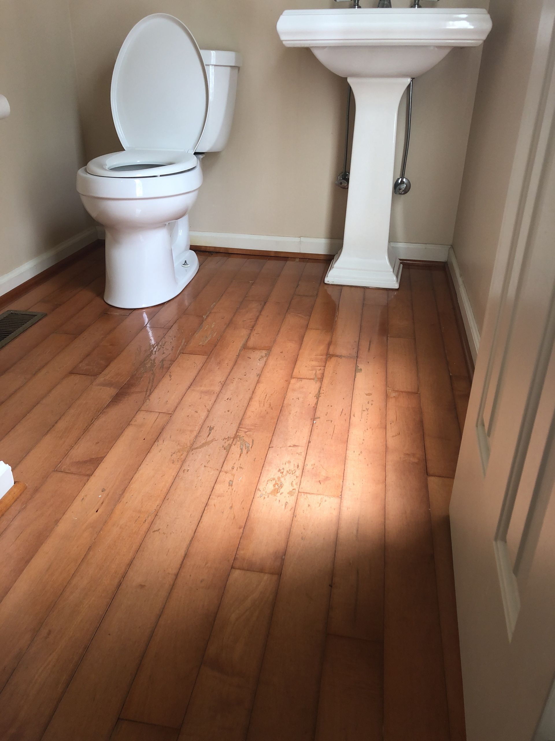 Bathroom with a white toilet, sink, and wood floor. Hardwood sanding and refinishing Cary NC.