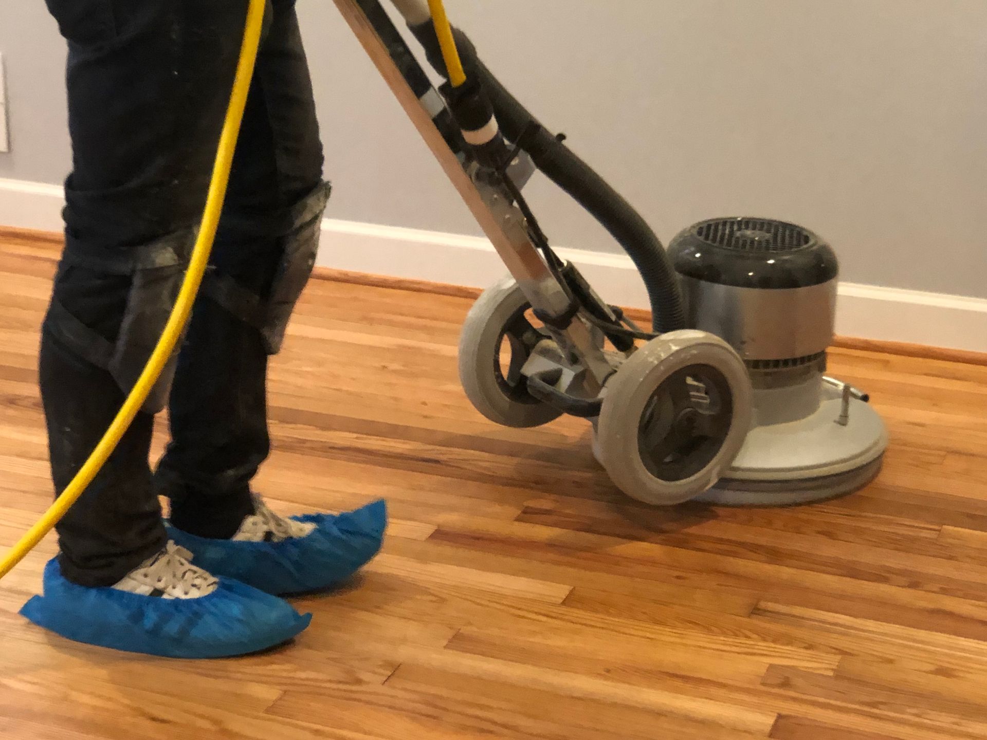 A person is using a machine to apply natural oil finish to a wooden floor
