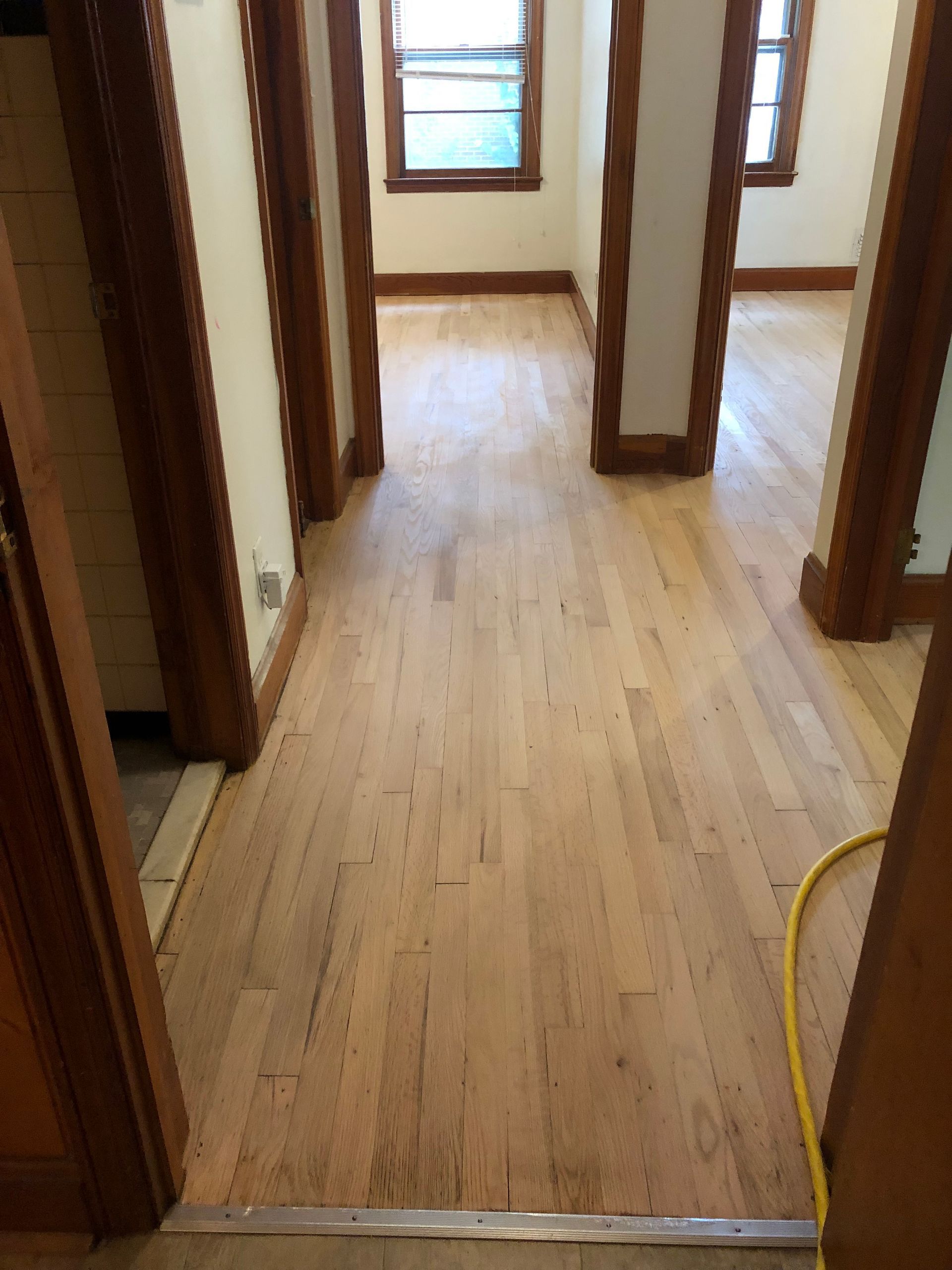 Hardwood floor hallway with dark wood trim, leading to windows.