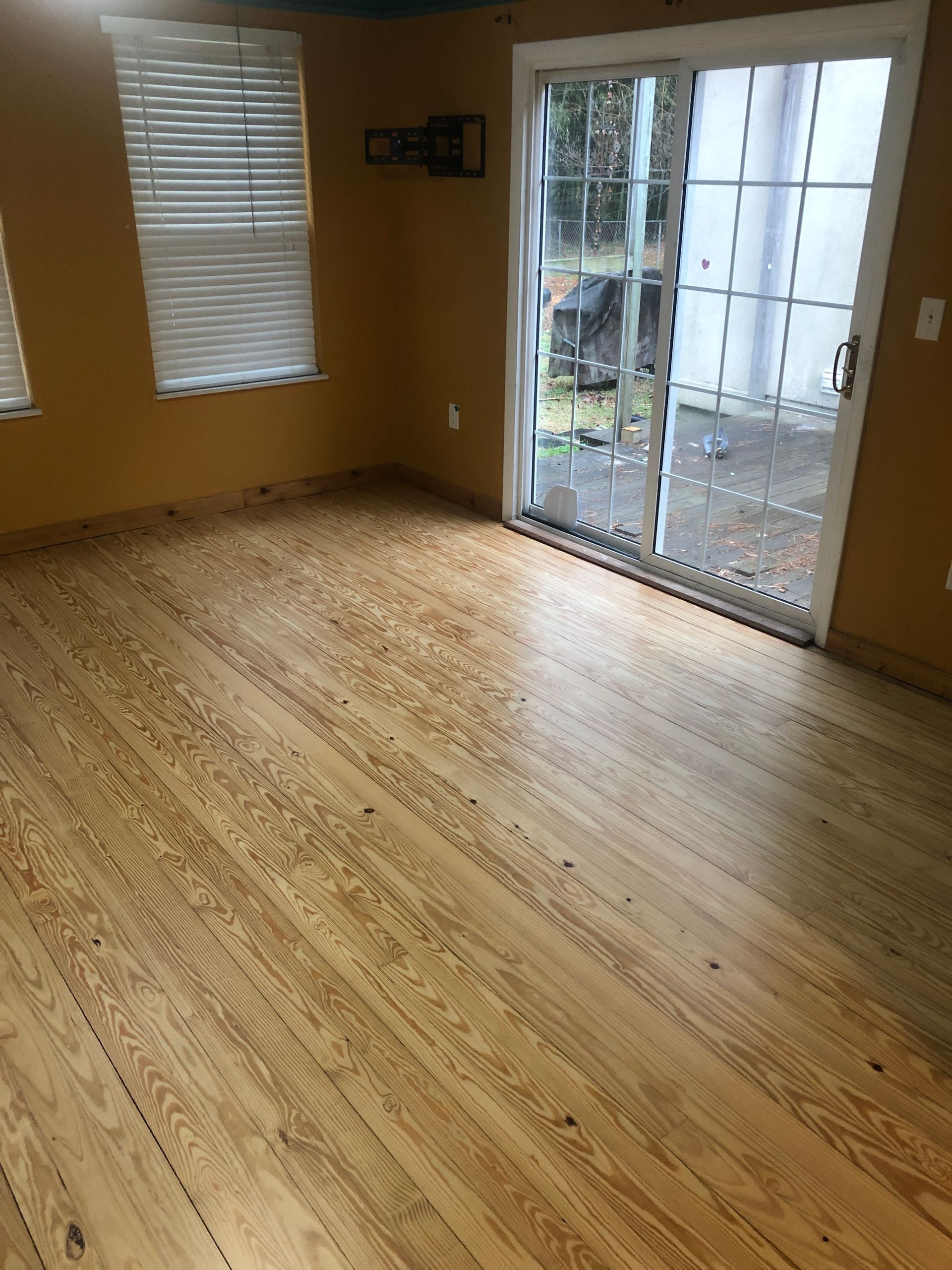 Empty room with hardwood floor, tan walls, window blinds, and sliding glass doors to a patio
