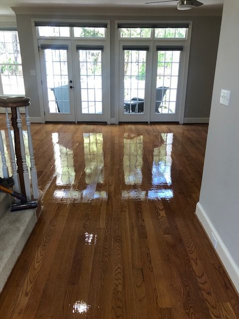 Shiny, newly-finished hardwood floor reflects light from windows and doors in a bright interior.