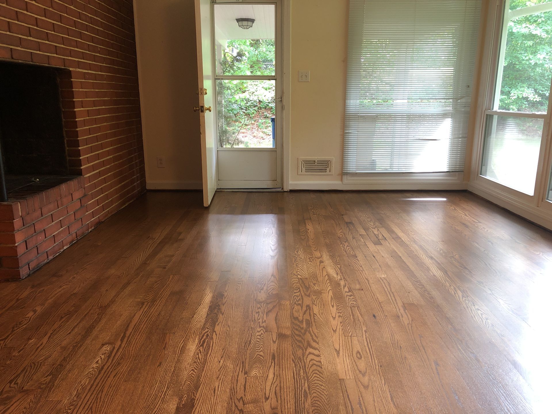 An empty living room with natural oil finished hardwood floors and a fireplace.