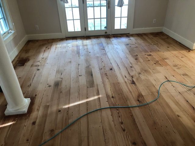 Wood floor in room with white trim, doors, and a pillar; a green cord lies across the floor.