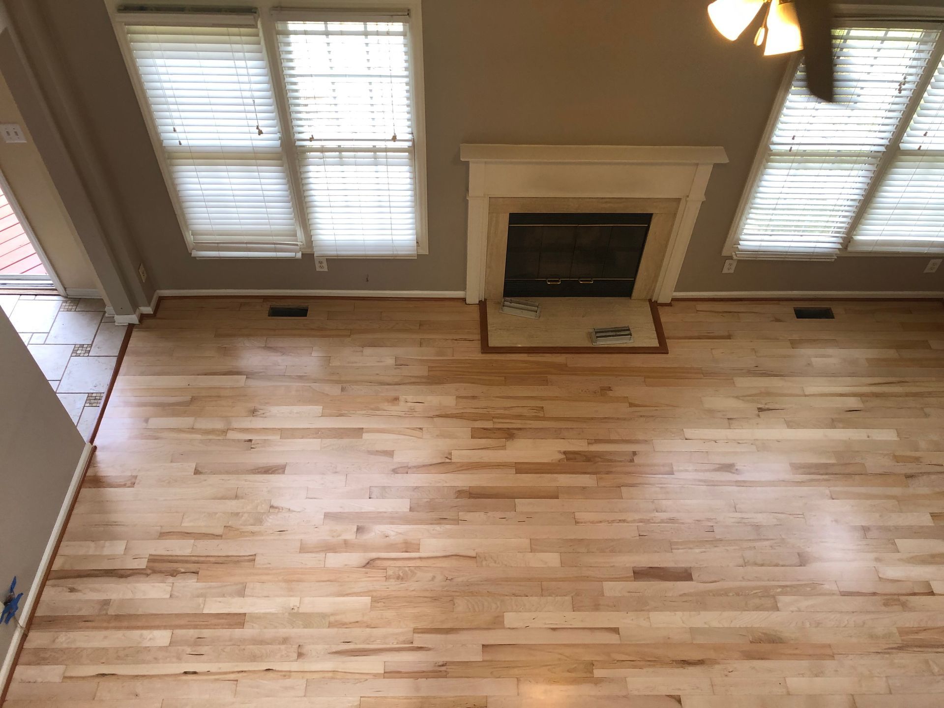 Empty room with light wood floors, a fireplace, and two windows with blinds.