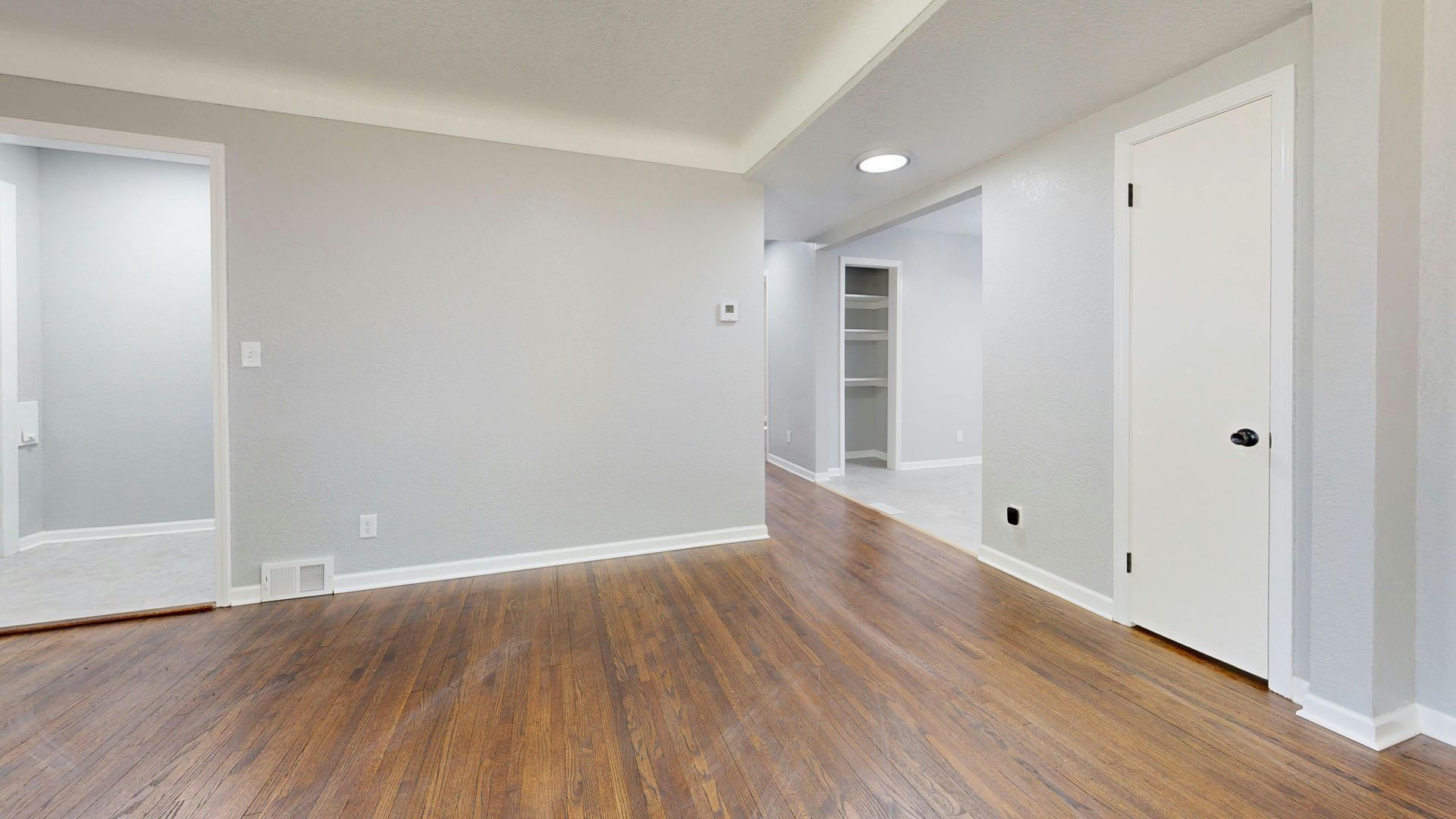 Empty room with hardwood floors, white trim, and gray walls; doorway on the left, door on the right.