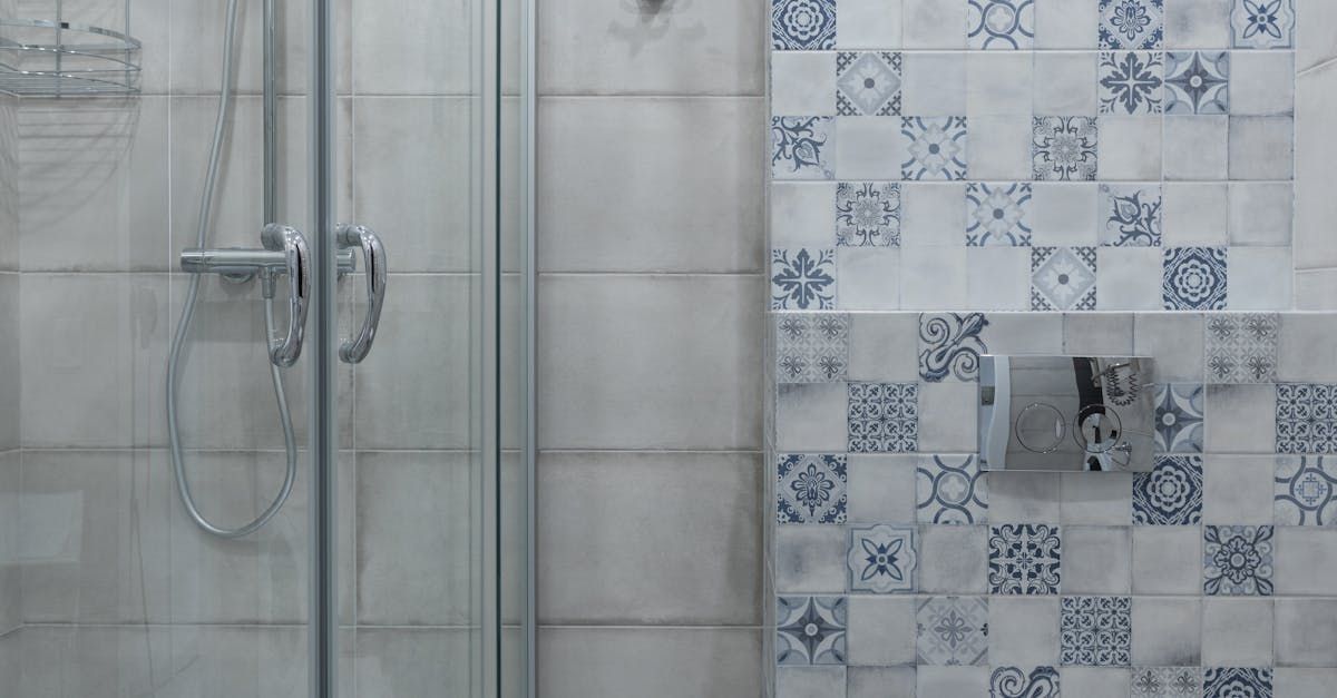 Shower with glass door, tiled walls. Blue and white patterned tiles contrast with gray tiles.