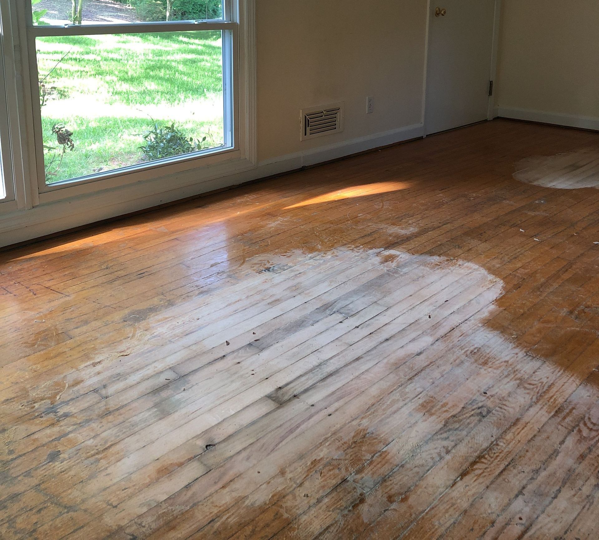 A room with a wooden floor partially sanded and a window.