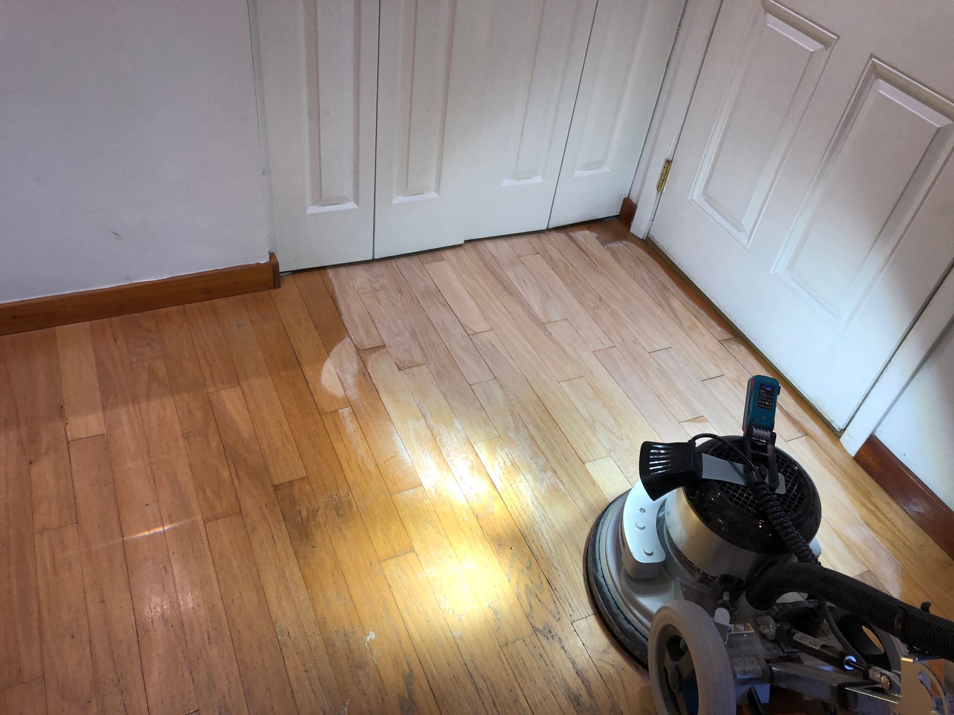 A hardwood floor sander is sanding a wooden floor in a room.