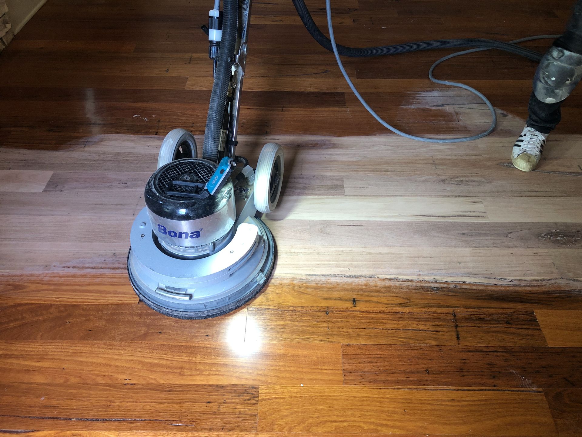 Floor sander on hardwood floor, sanding process, dark stained wood to raw wood.