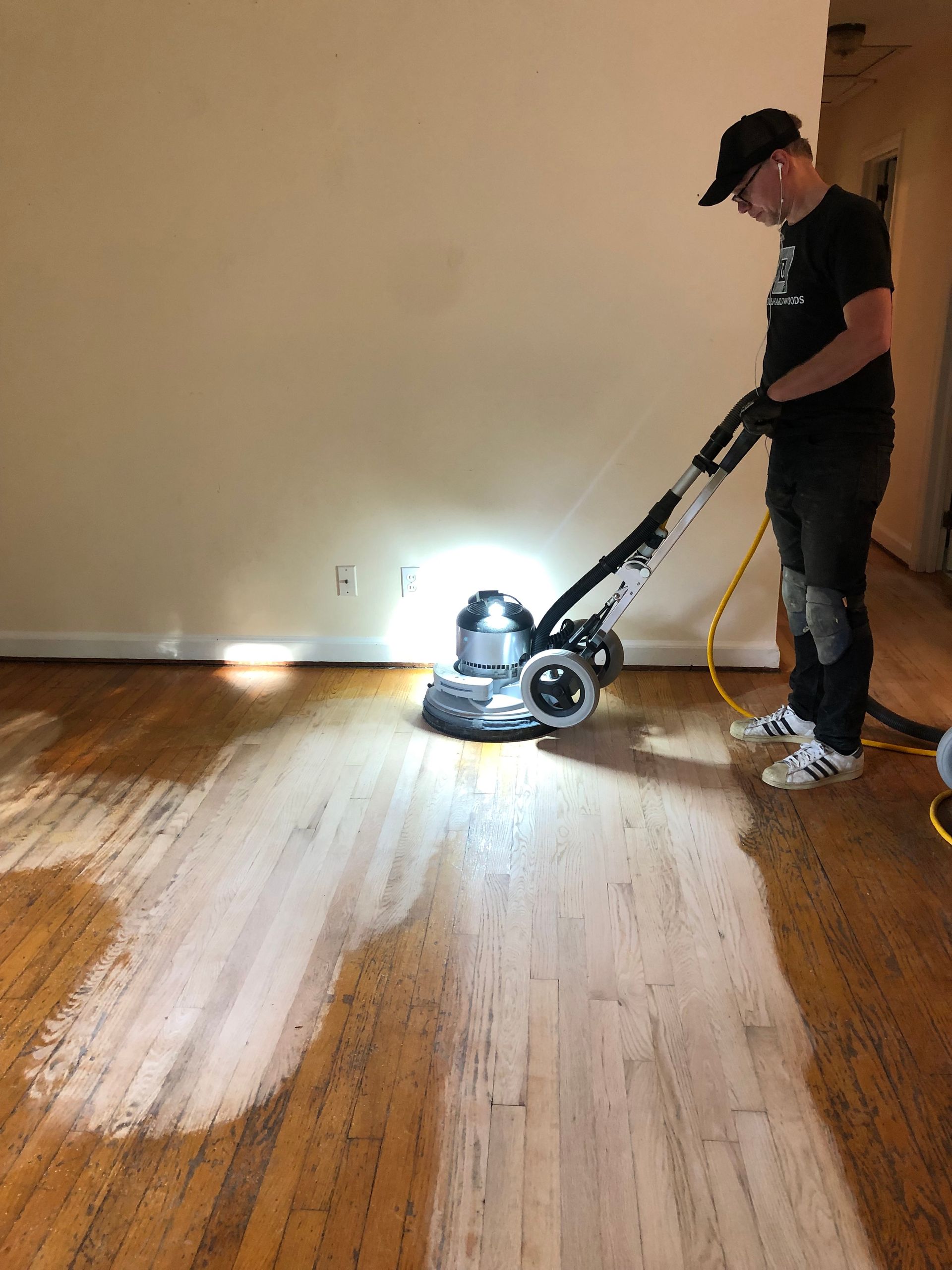 Person using a floor sander on a hardwood floor in a sparsely furnished room