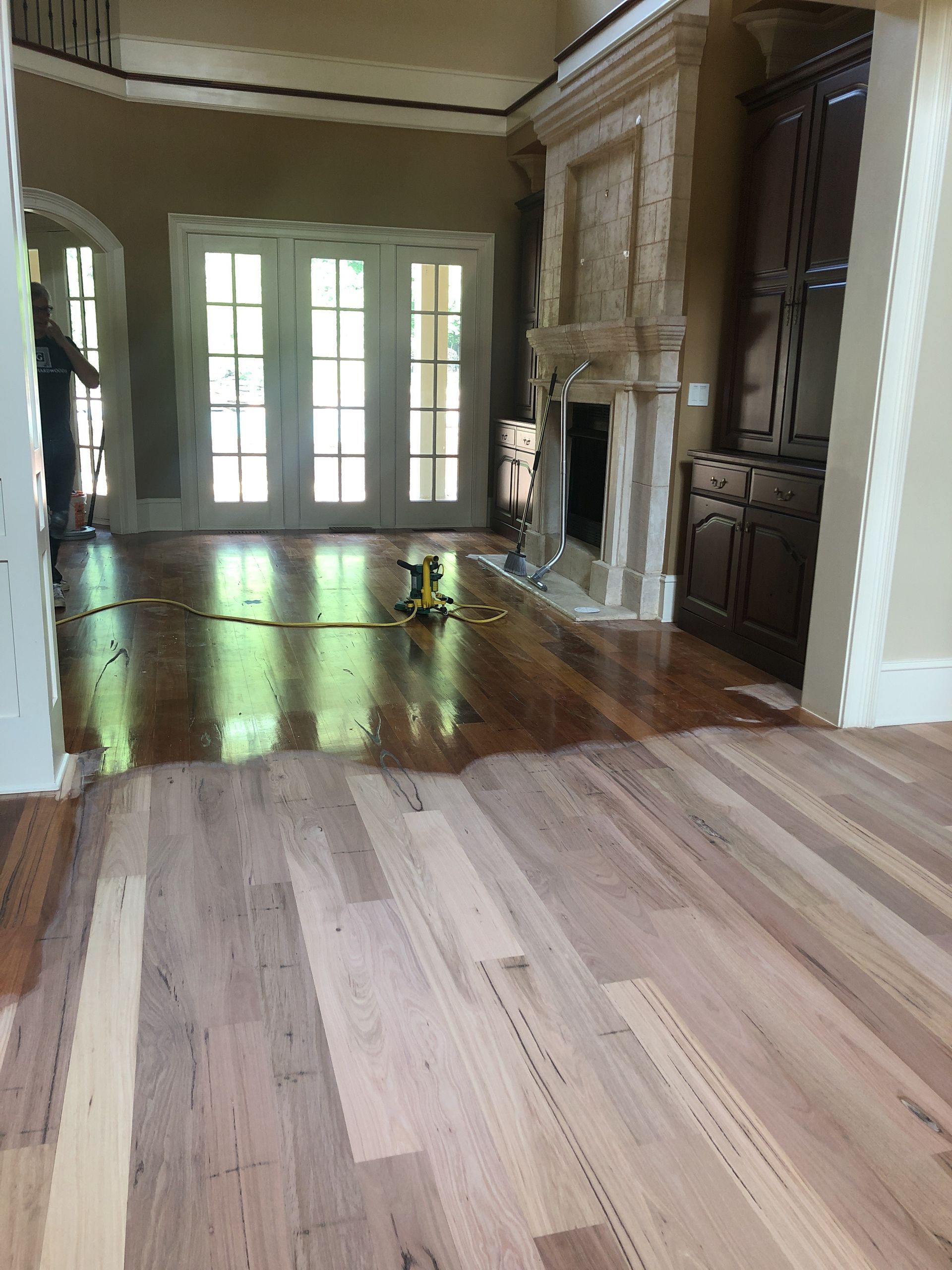 Hardwood floors refinished in a room with French doors, a fireplace, and cabinets. Sunlight reflects on the polished surface.