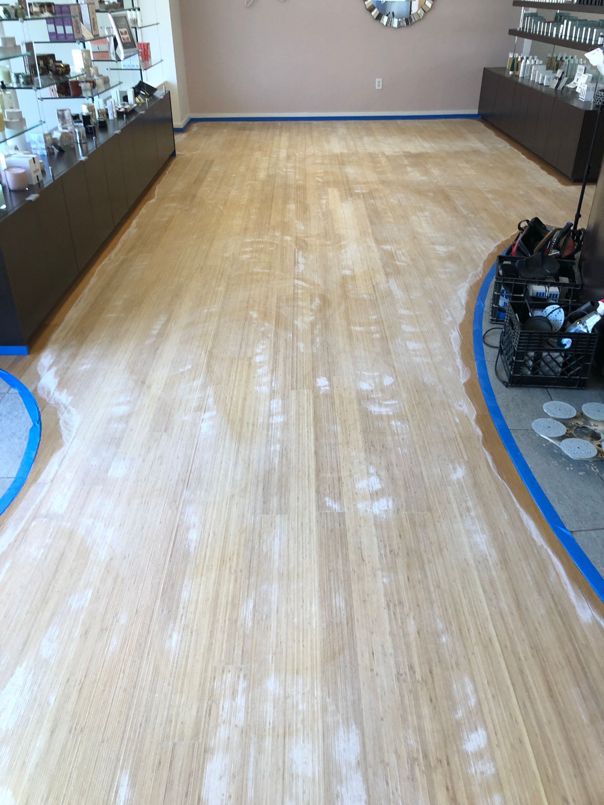 Wooden floor being refinished with sanding residue, taped off around shelves and fixtures. Synergy Spa Raleigh NC.