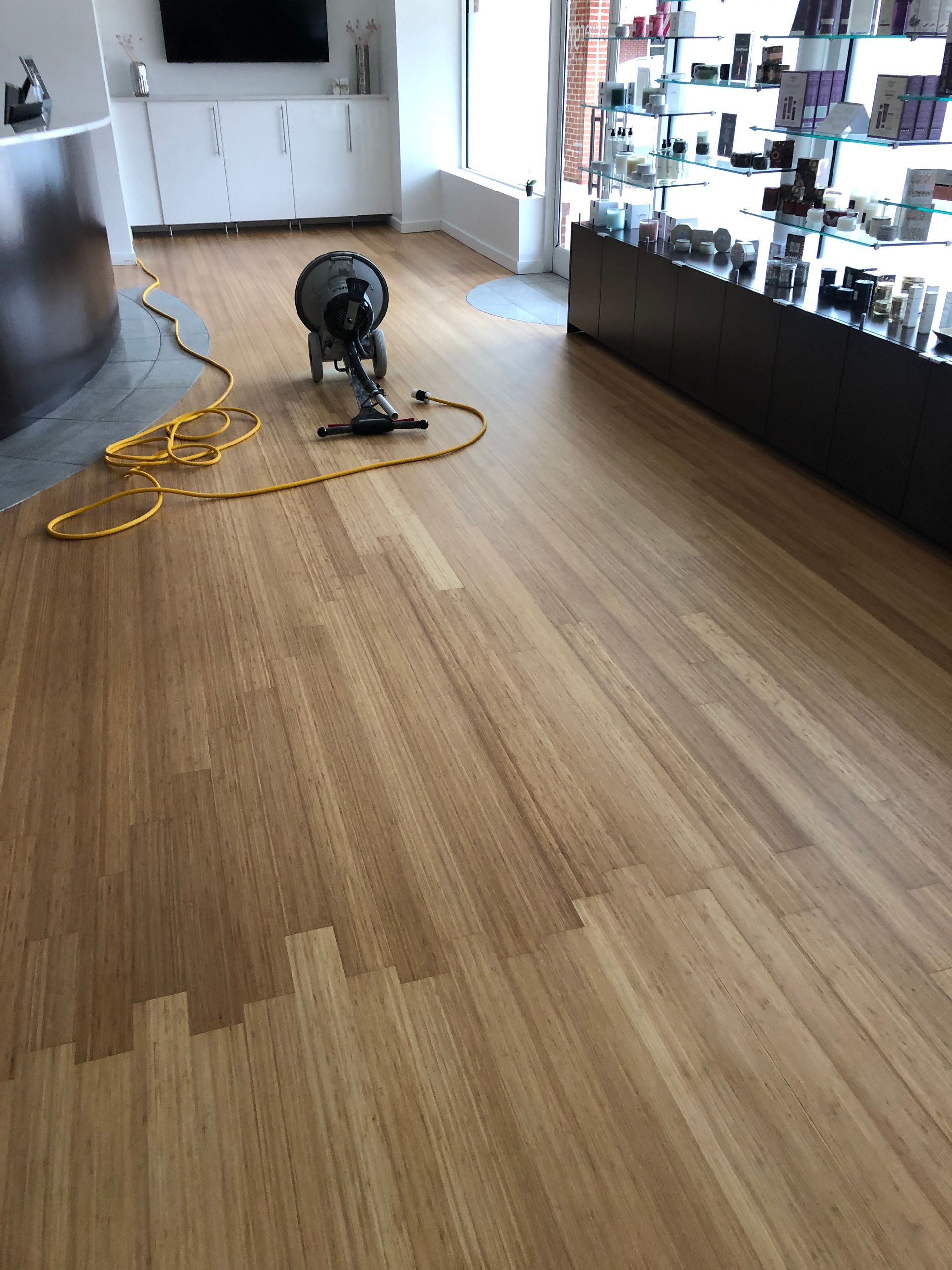 Bamboo floor being buffed with a machine at Synergy Spa Raleigh NC, with a display case and cabinetry in the background.