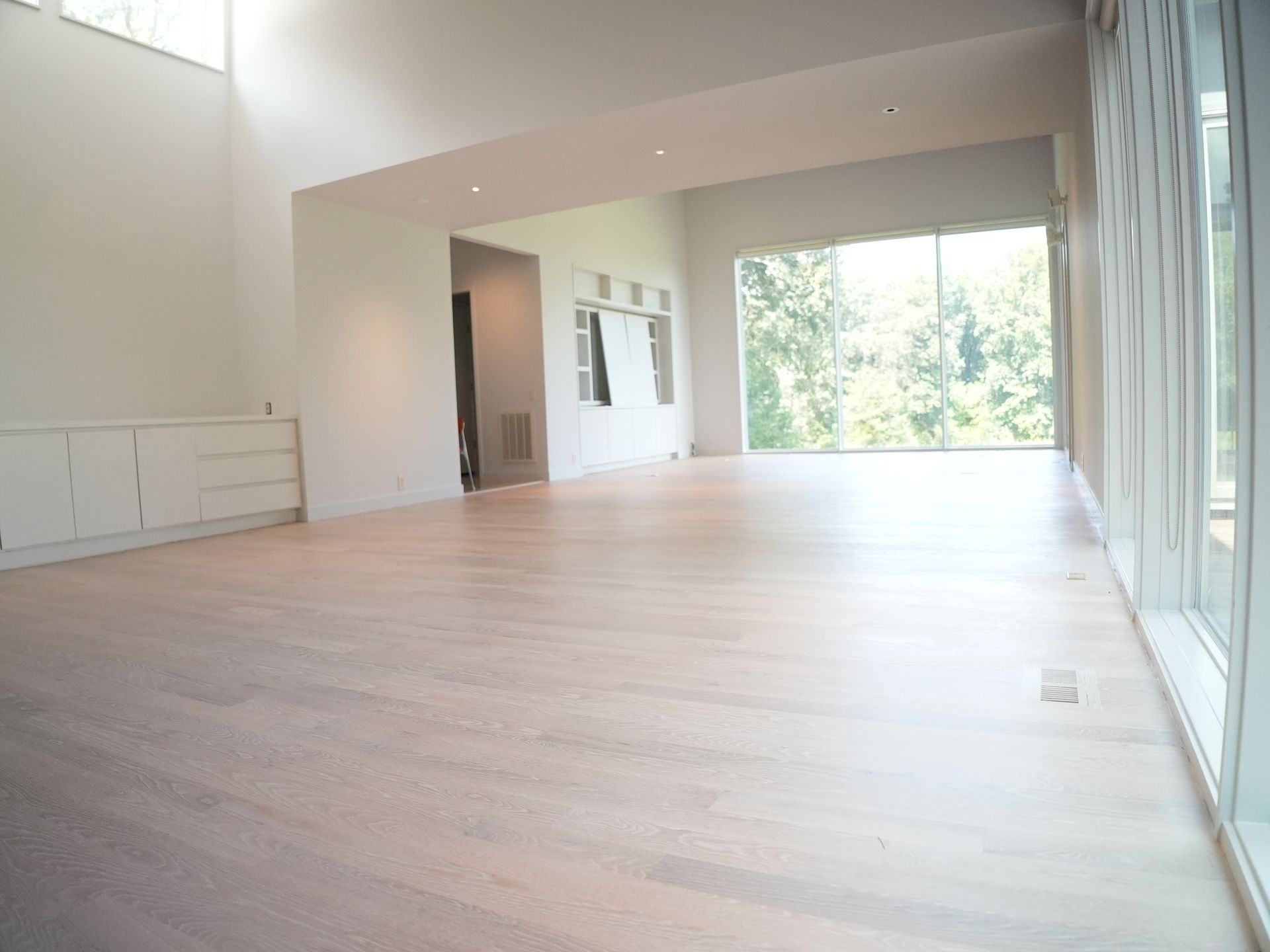 A large empty room with white oak hardwood floors and lots of windows.
