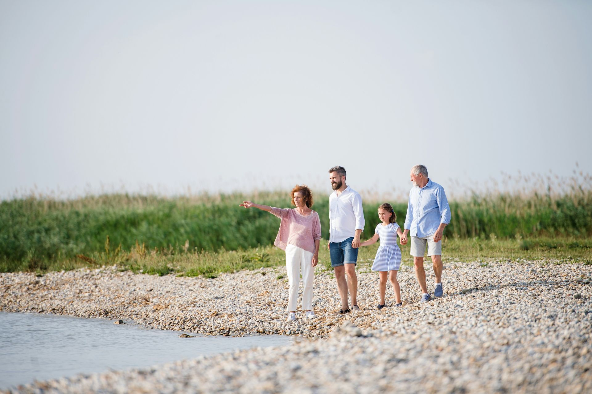 Family on a rocky beach; woman points, others walk towards water on a sunny day.
